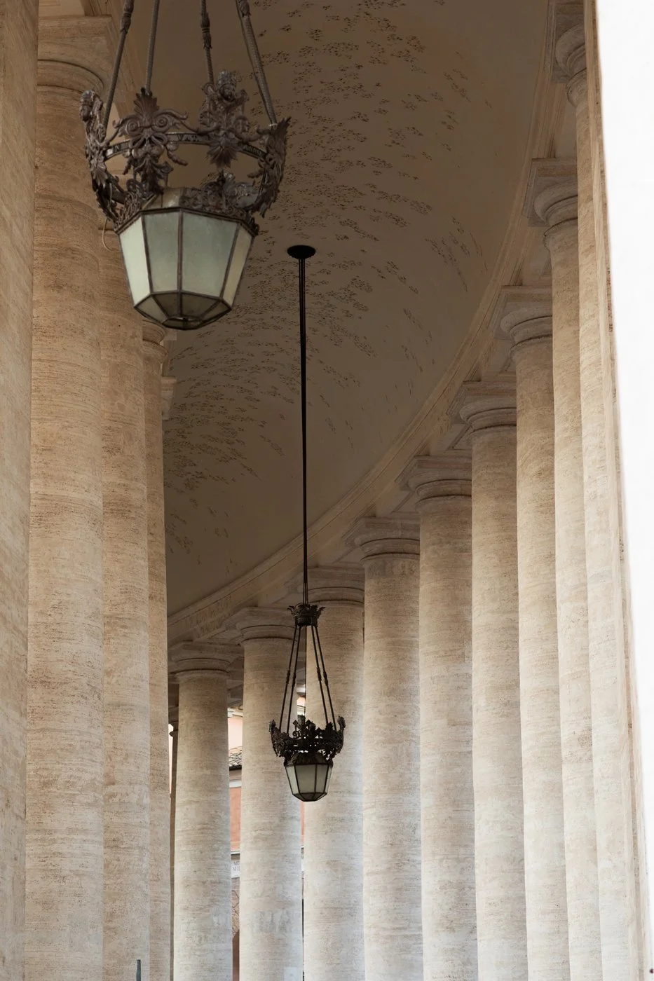 Tall stone columns with classical design supporting a curved ceiling, with ornate hanging lanterns.