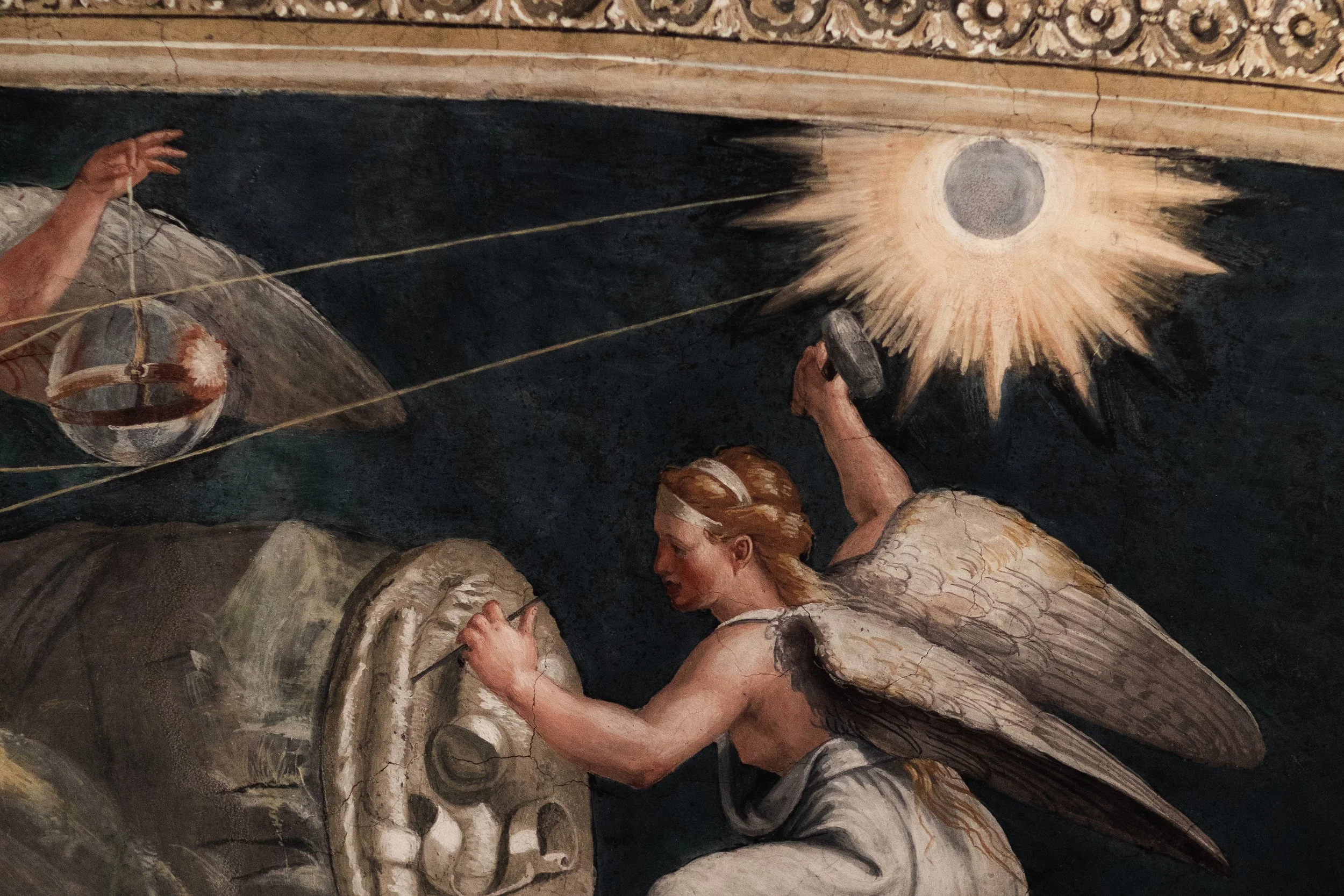 Close-up of a religious painted ceiling showing angelic figures with wings, one holding a drum, and a luminous celestial object in the background.
