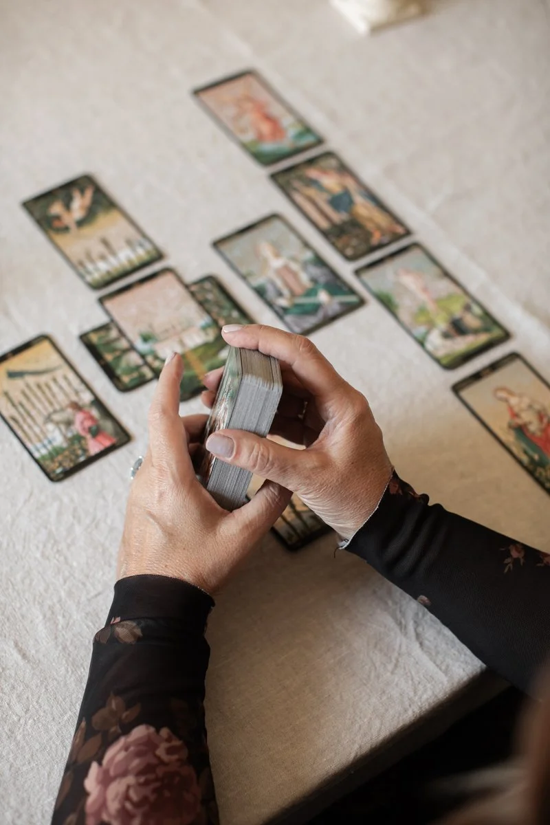 Person holding a tarot deck while shuffling cards on a table, with tarot cards laid out in a spread.