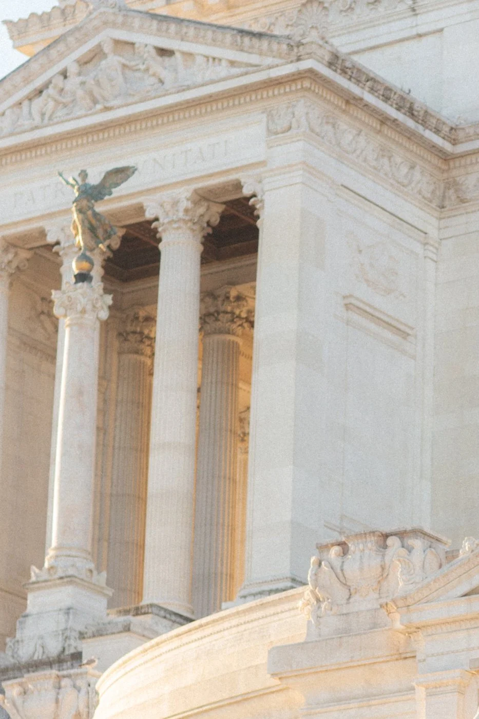 Close-up of the Roman Pantheon with columns, detailed carvings, and a sculpture of a winged figure on top.