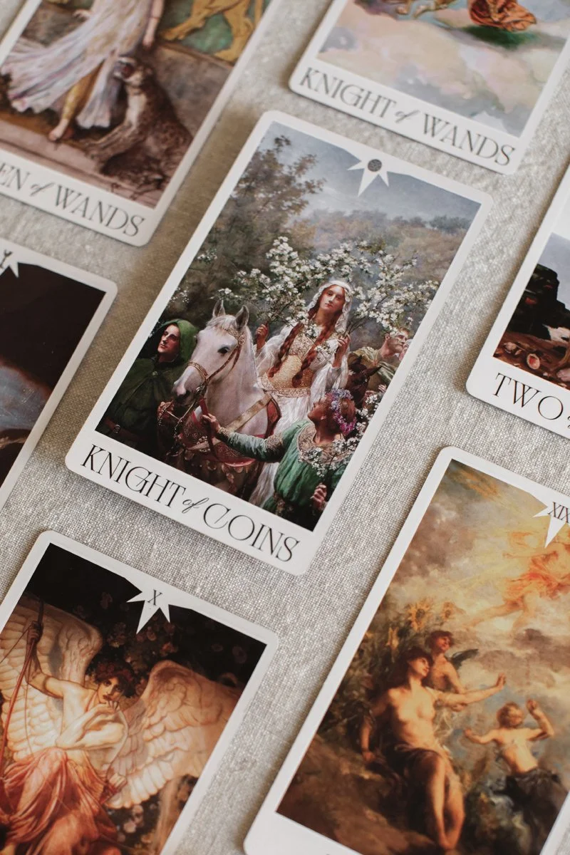 Tarot cards spread on a cloth, featuring various images including a woman on a horse with individuals around her, a mountain landscape, and a mythological figure with wings.