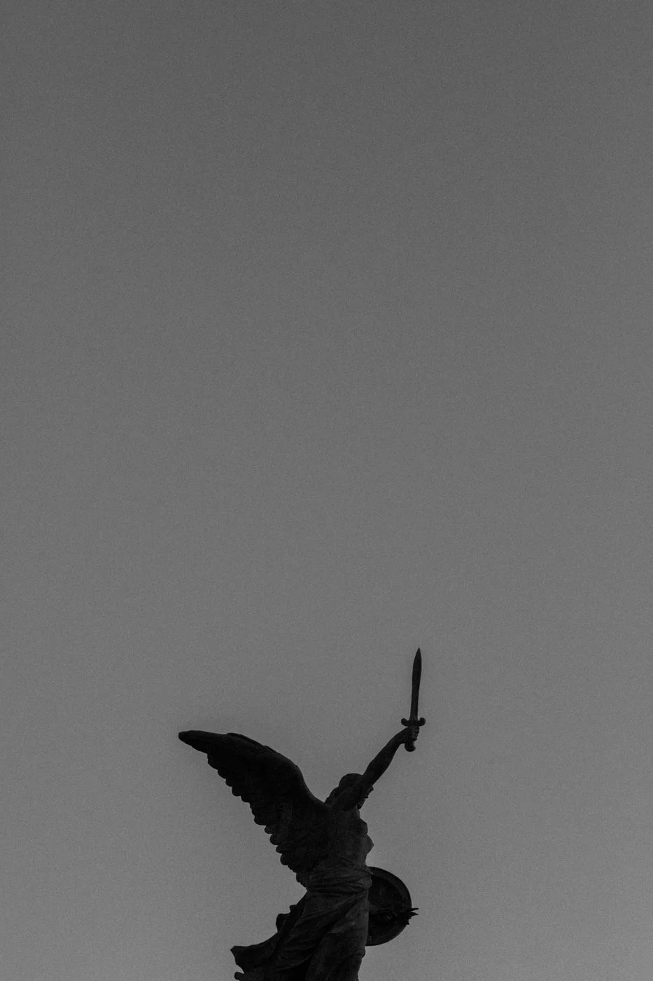 A statue of the angel of Independence holding a sword, set against a gray sky.