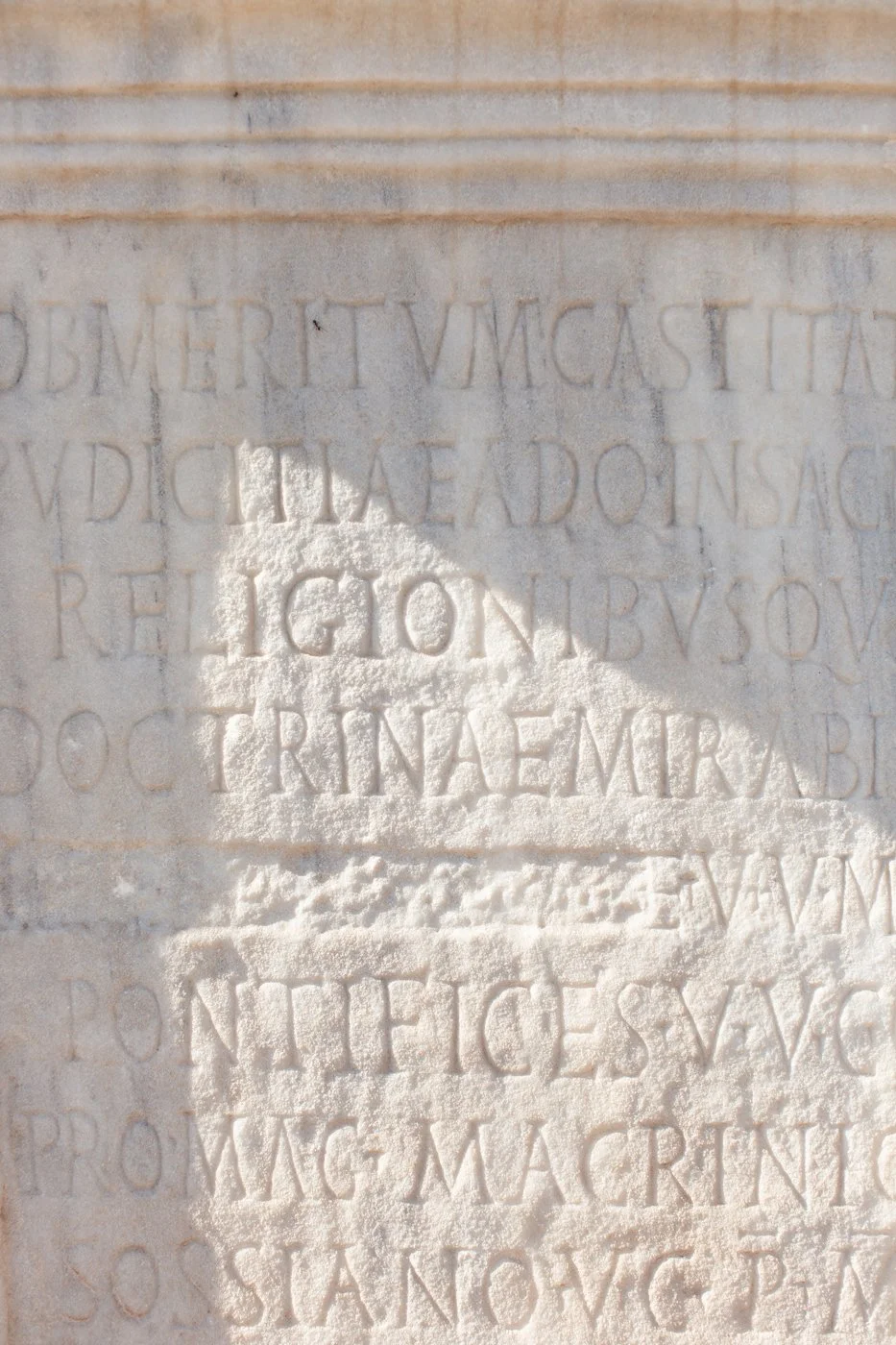 Close-up of a stone wall with Latin inscription carved into it, partially illuminated by sunlight.