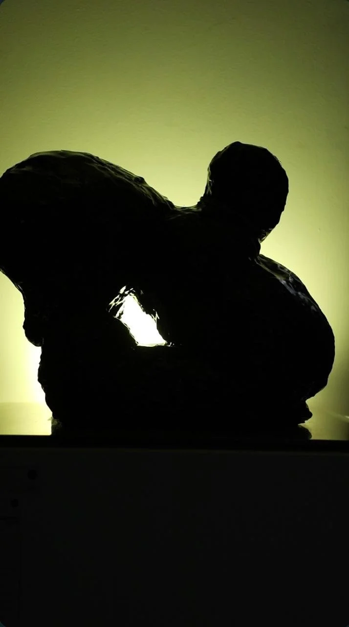Silhouette of a person kneeling and leaning forward, backlit with a bright yellow-green background.