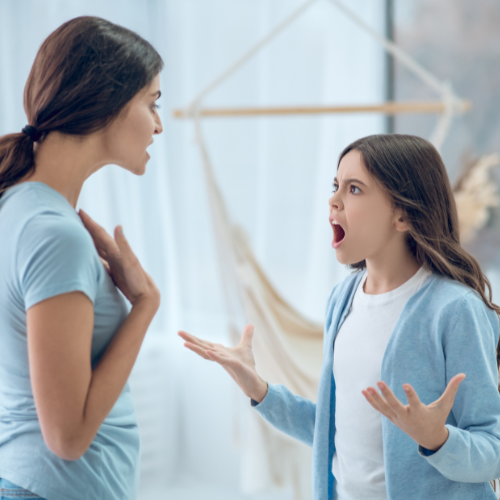 Madre e figlia in lite, madre con mano sul petto, figlia arrabbiata con le braccia alzate.