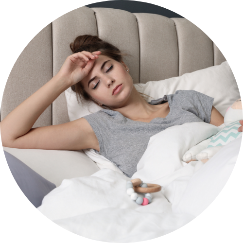 Una giovane donna distesa a letto, apparentemente stanca o malata, che si tiene la fronte con una mano.