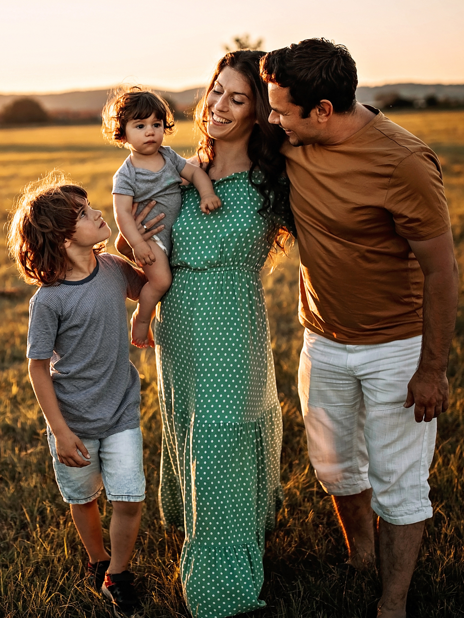Una famiglia che cammina insieme in un campo durante il tramonto, sorridendo e condividendo un momento di felicità.