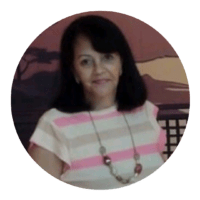 Donna con capelli scuri, indossa una maglietta con righe rosa e bianco e una collana, sfondo con cielo e silhouette di edifici.