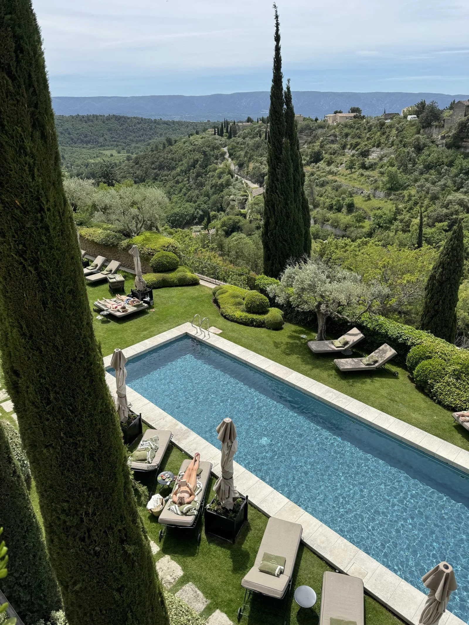 A serene view of a rectangular pool surrounded by manicured green lawns and sun loungers.
