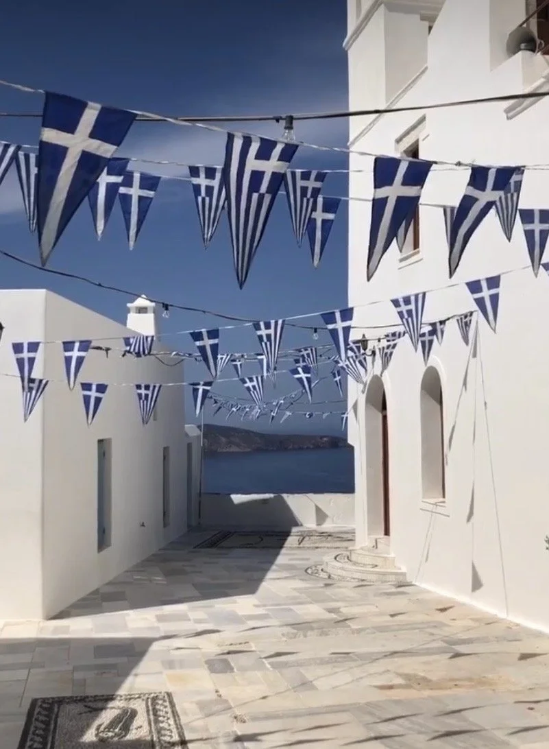 Narrow alley in a Greek village, adorned with blue and white flags under a clear sky.