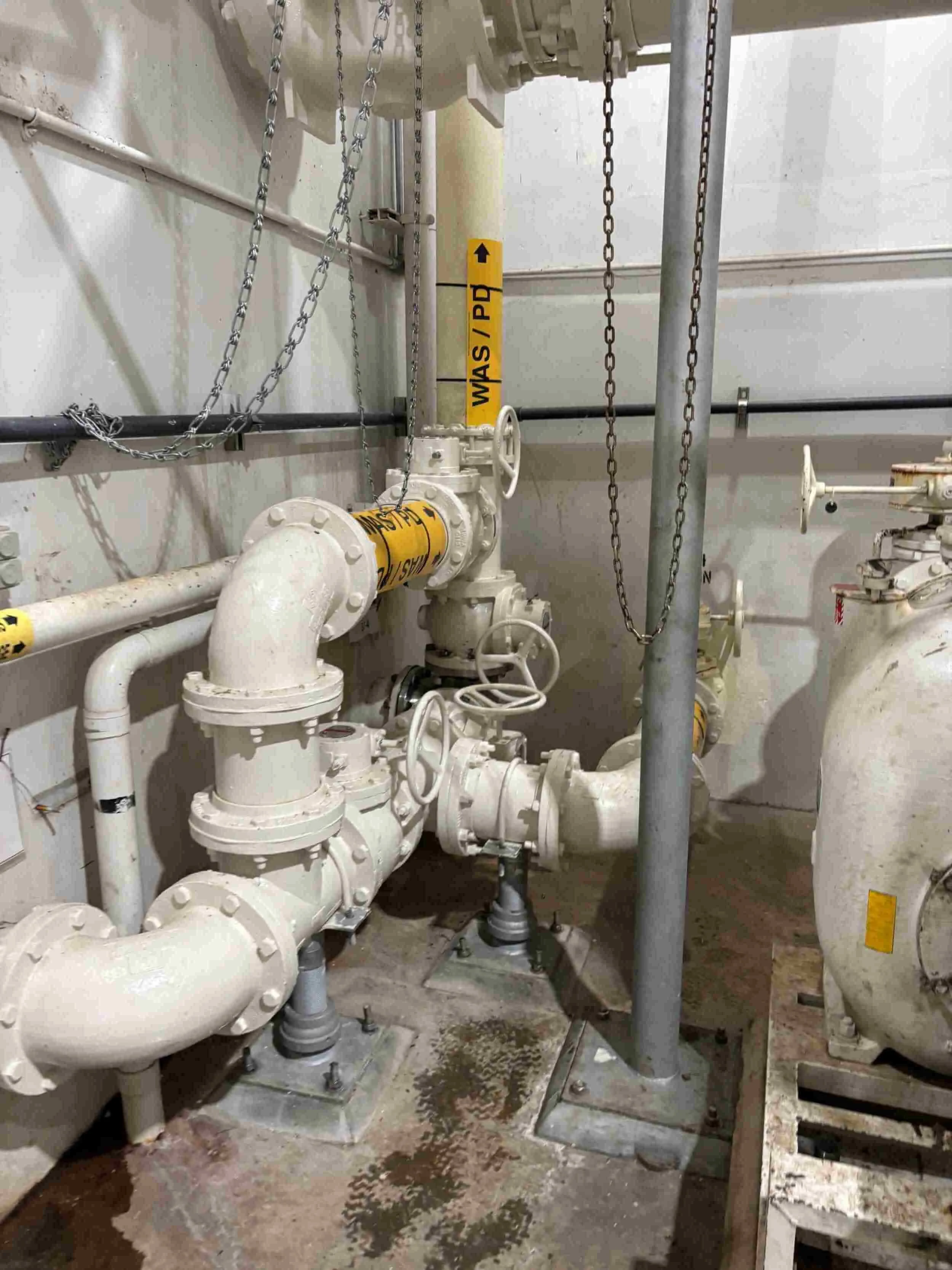 Industrial piping system with valves, chains, and yellow safety labels indicating WASH/PD.