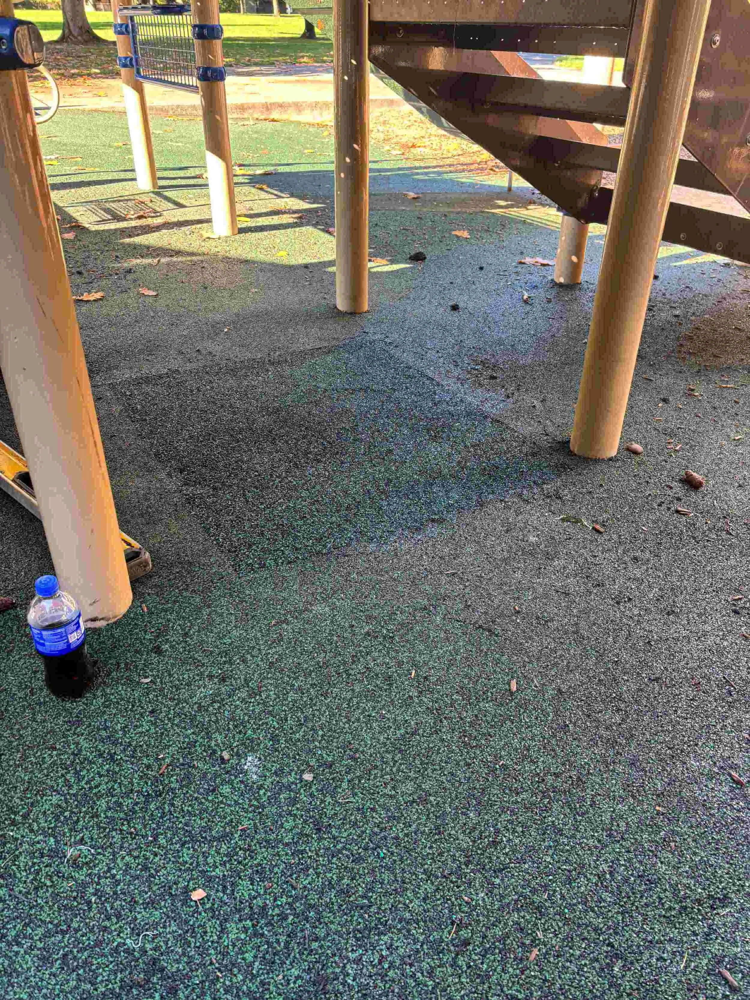 Spot of spilled liquid on playground rubber flooring near playground equipment at a park.