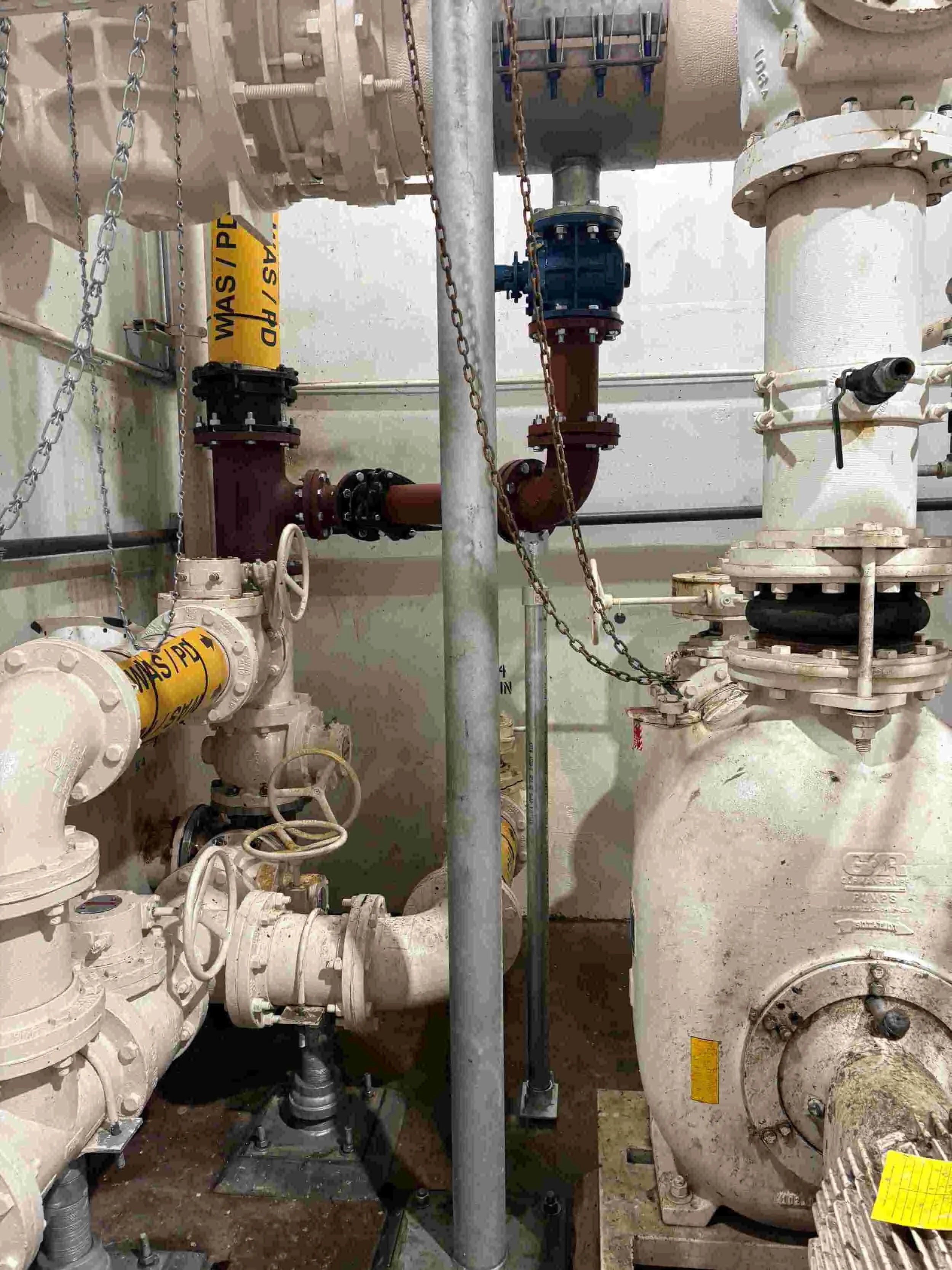 Industrial piping system with valves, pipes, and chains in a mechanical room.