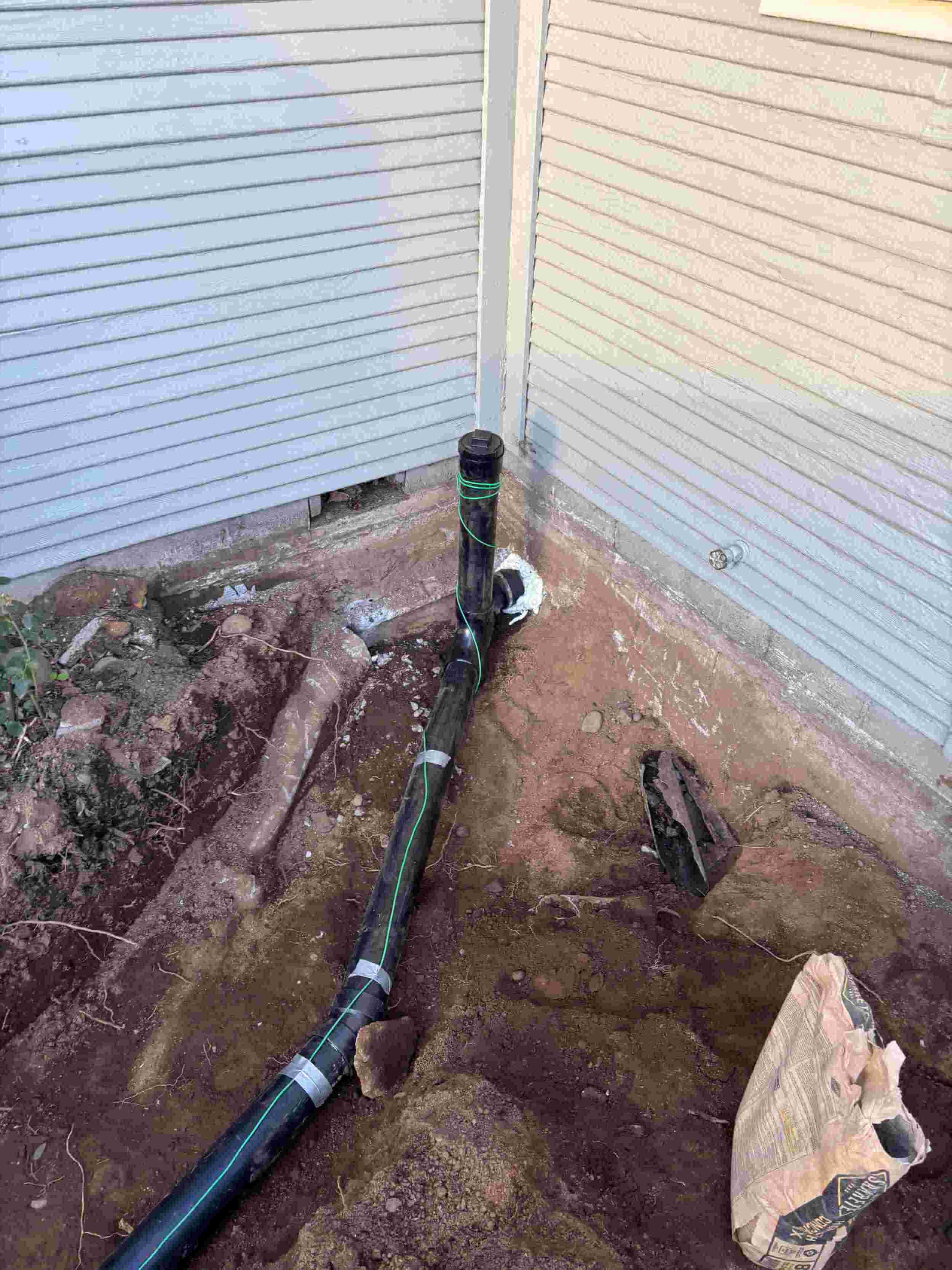 Underground plumbing pipe installation next to siding exterior wall.