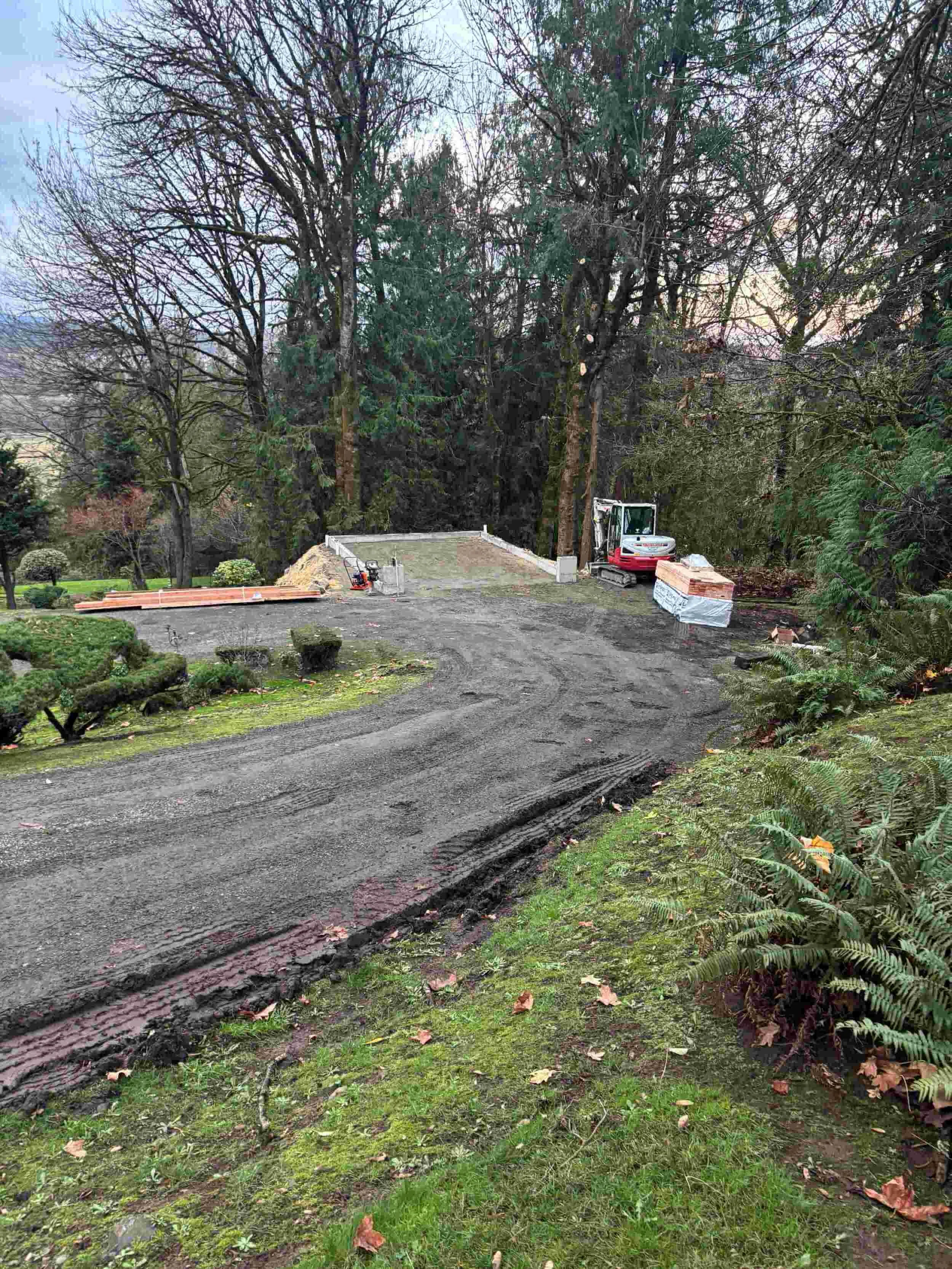 Landscaping in progress in a garden area with dirt ground, a small excavator, and trees in the background.
