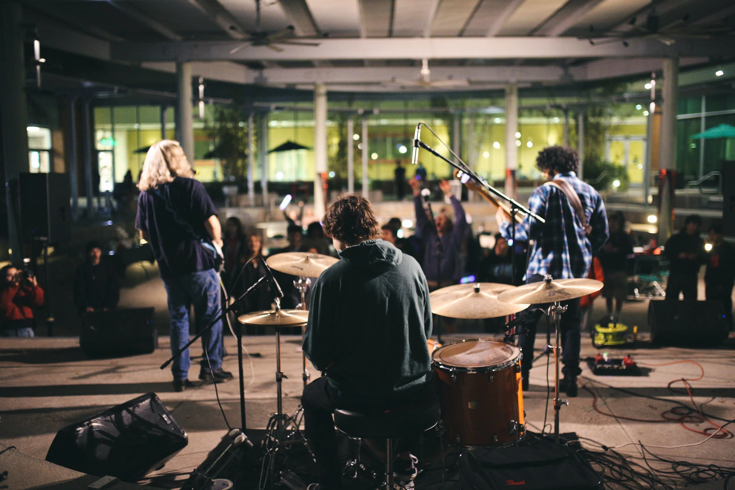 A band performs on a stage in an indoor venue with audience members watching and enjoying the music.