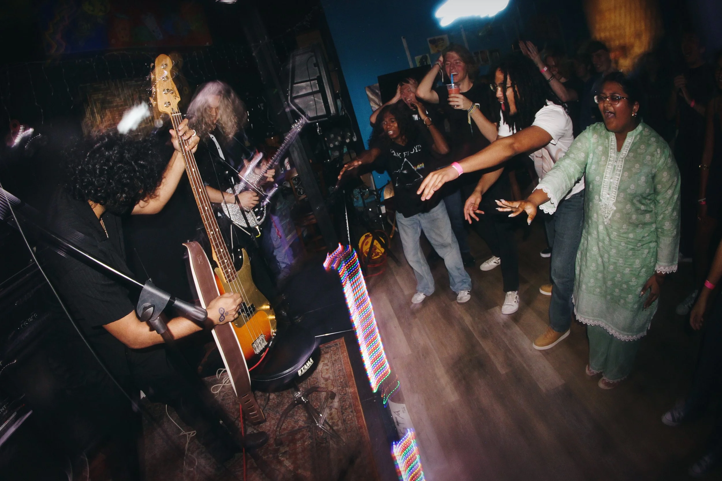 People dancing and enjoying live music performance in an indoor venue, with two musicians playing guitars on stage.