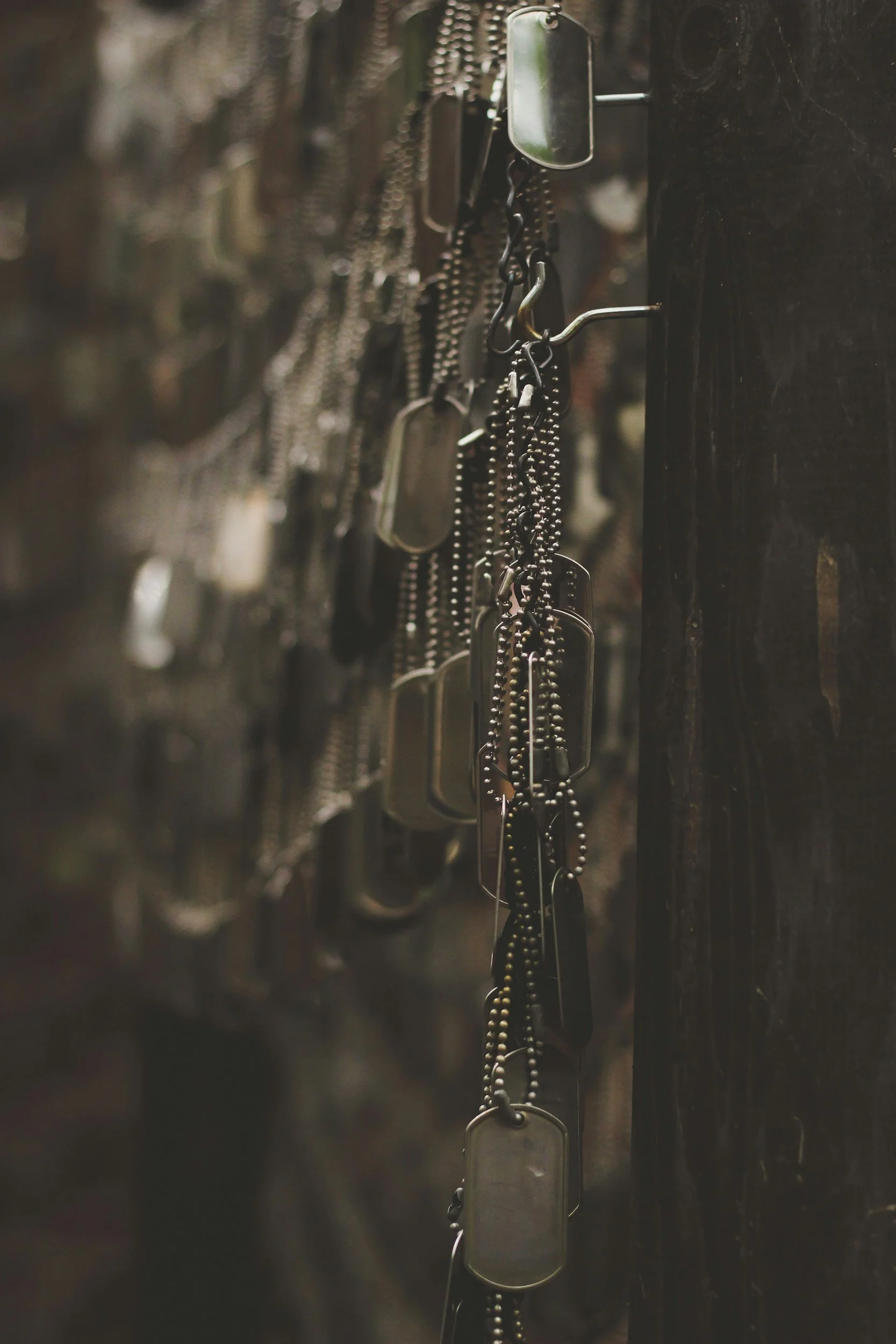 A row of military dog tags hanging on a hook against a dark background.