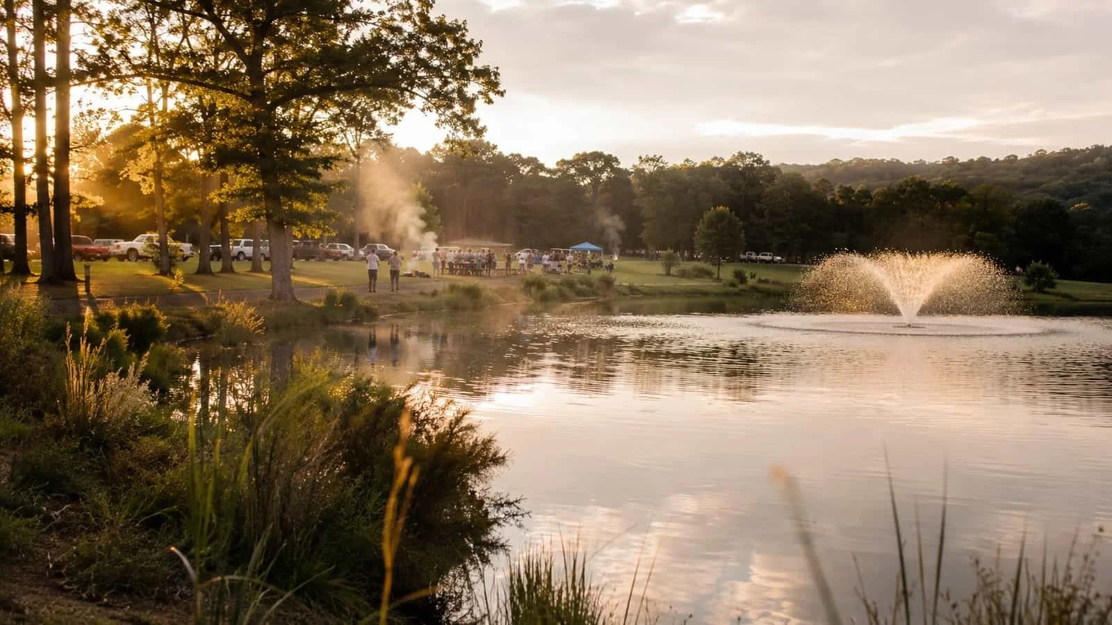 A clean community pond reflecting the sky at golden hour as families gather nearby for a cookout.