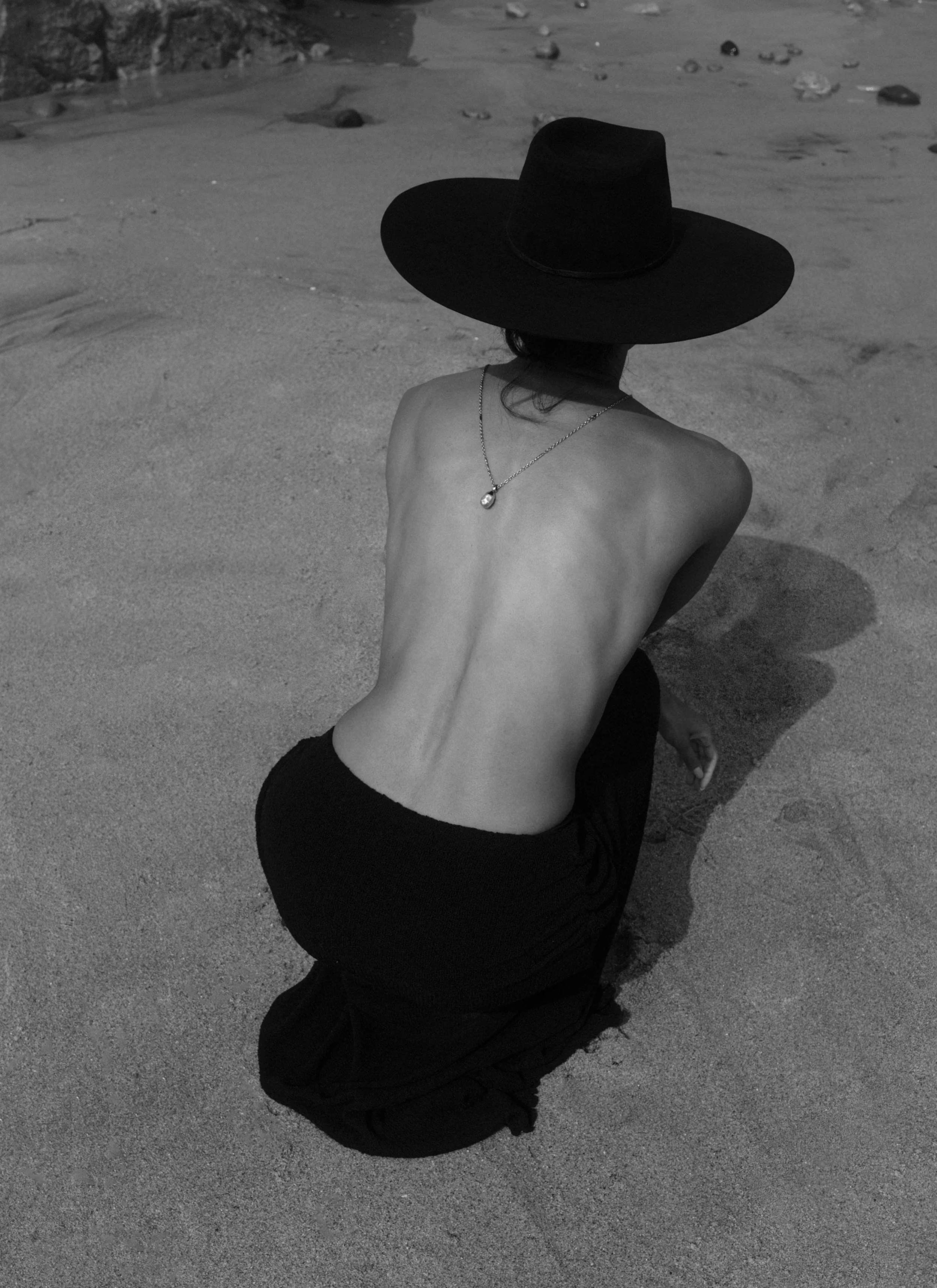 Woman on the beach wearing a black wide-brim hat by The Halo Lab