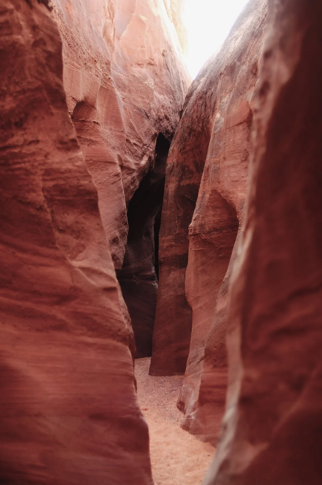 Narrow canyon walls with reddish-brown rock formations and a sandy floor, typical of slot canyons.