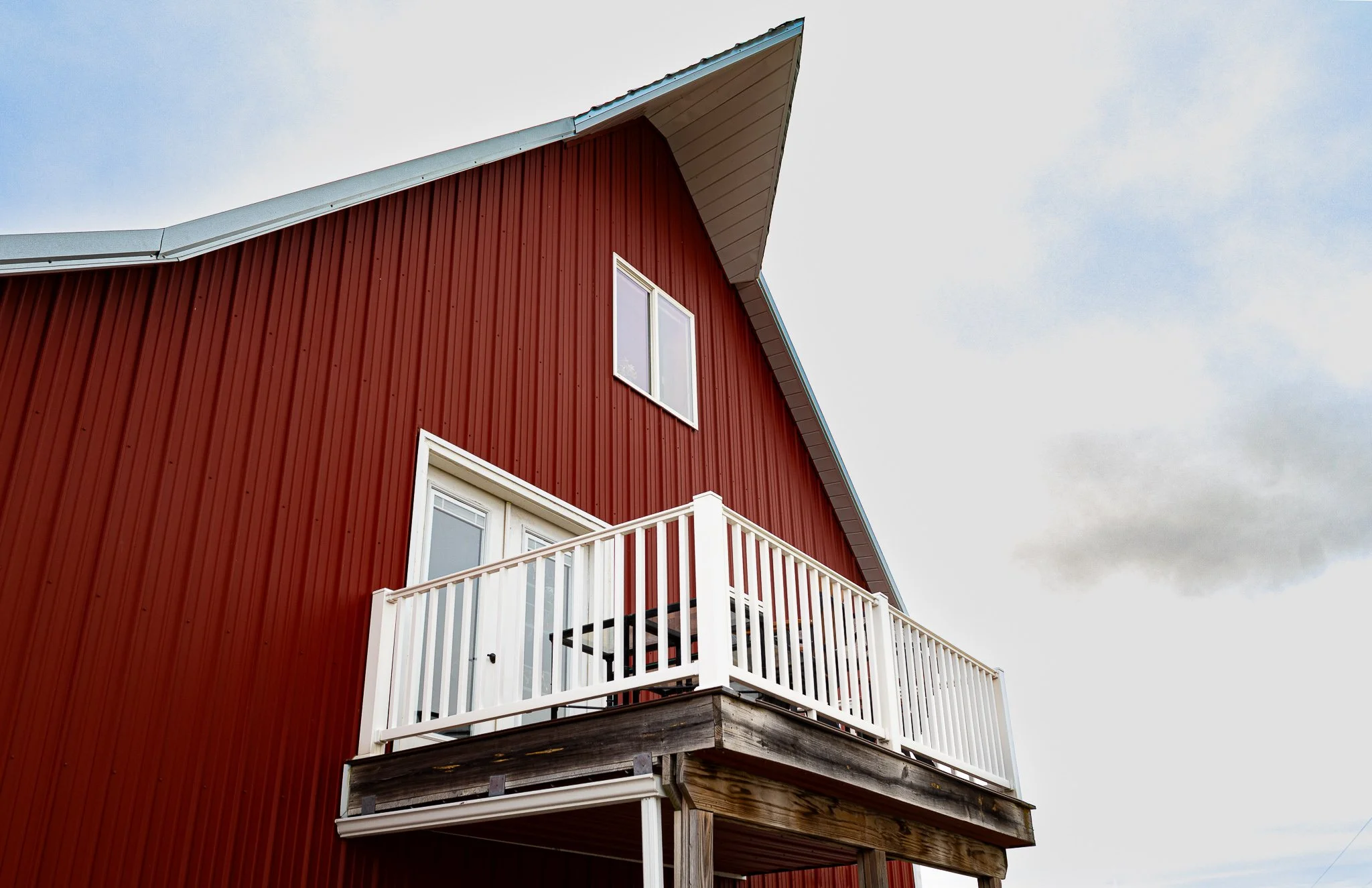 A red house with white framing, a balcony, and a sloped roof, under a cloudy sky.