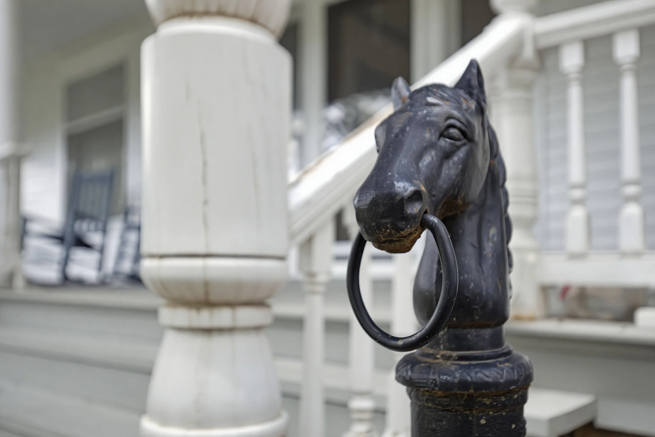 Close-up of a black horse head door knocker on a white porch railing.