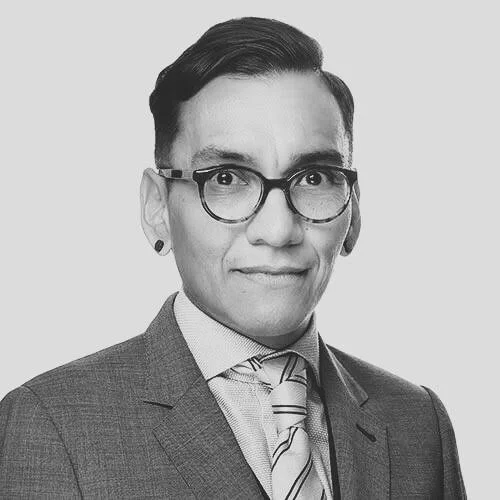 Black and white portrait of a person wearing glasses, a suit, and a striped tie, with short hair and a confident expression.