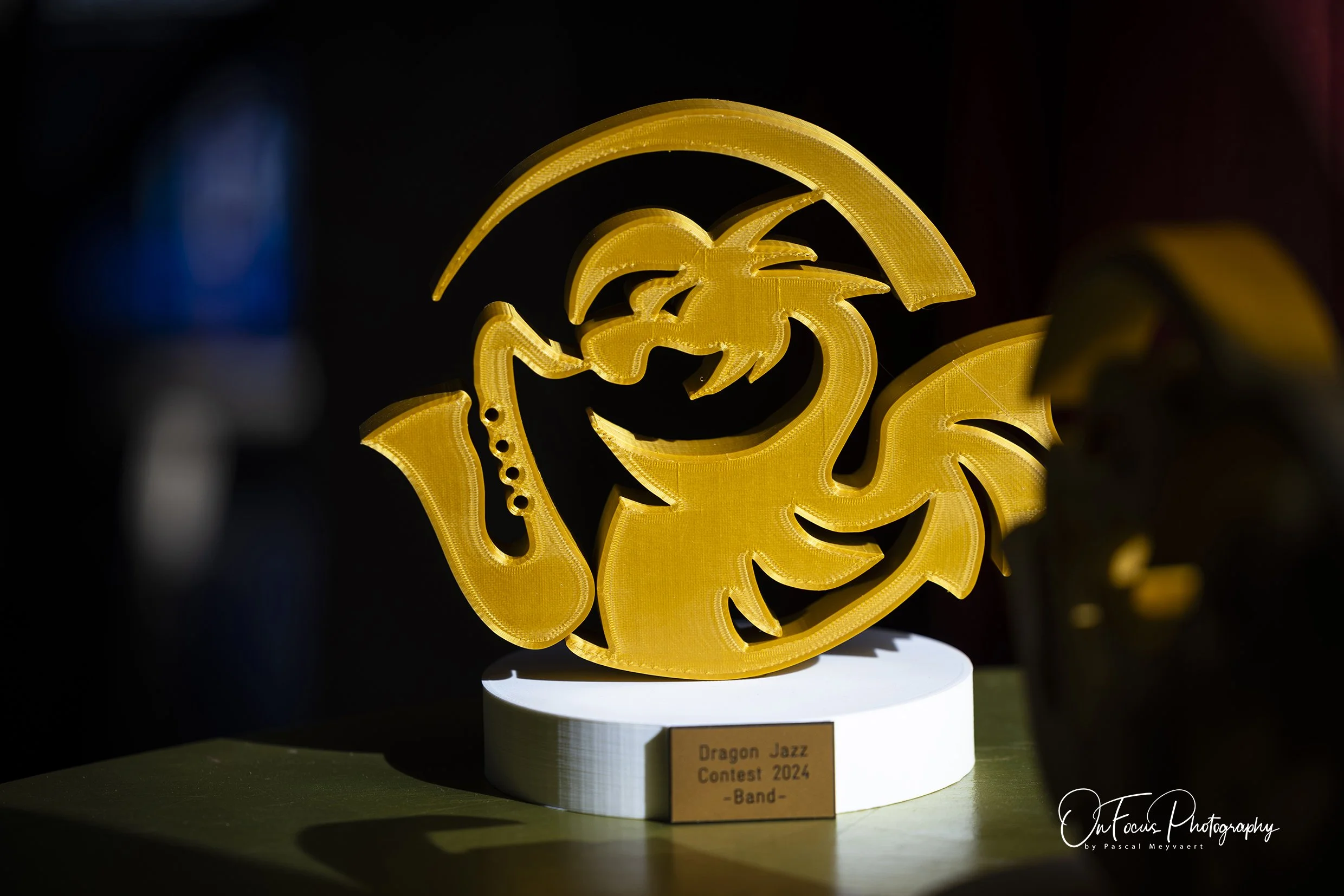 Gele LED-beeld van een draak, onderdeel van de Dragon Jazz Contest 2024, uitgestald op een witte standaard op een groene ondergrond.
