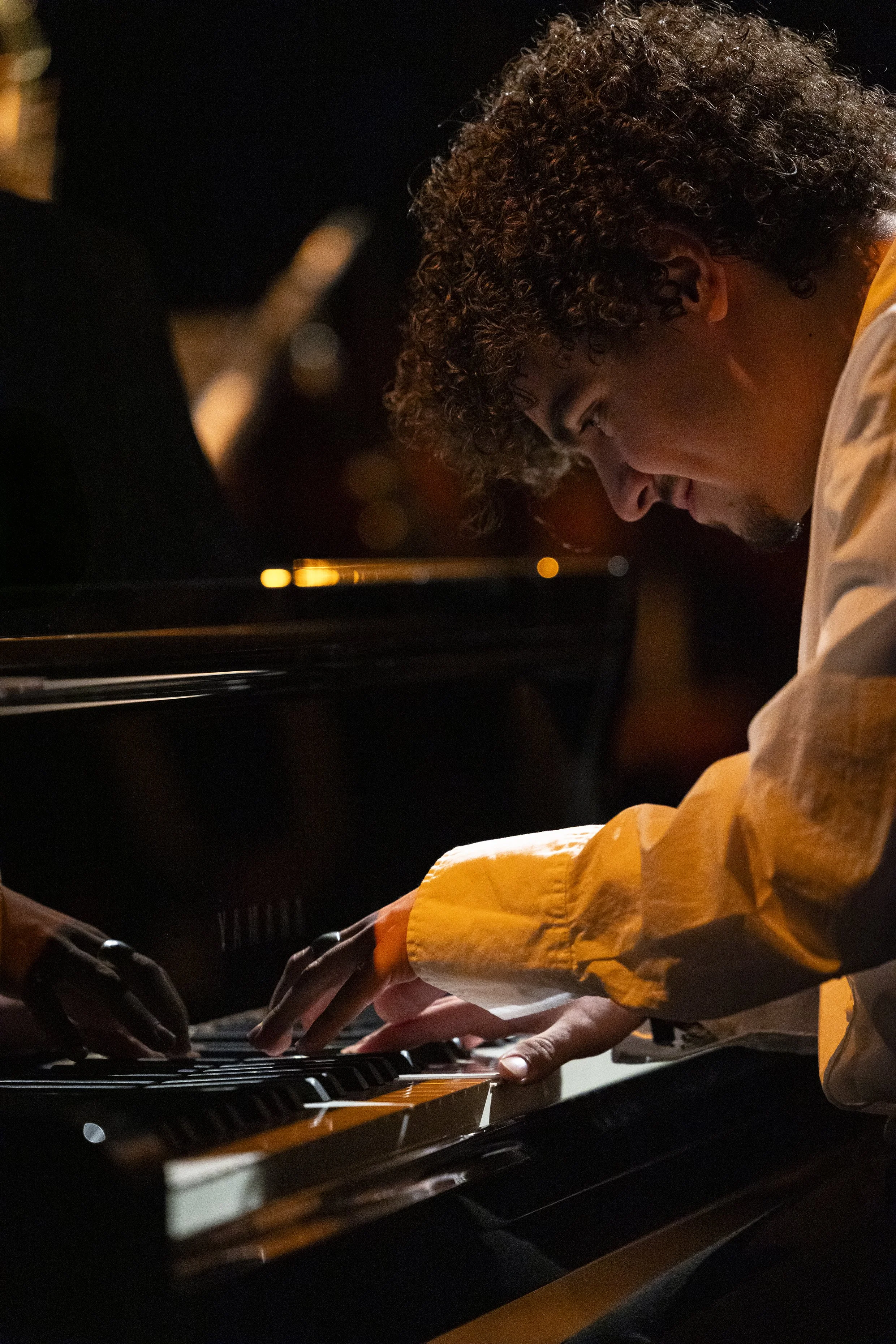Twee mensen spelen samen piano in een donkere ruimte.