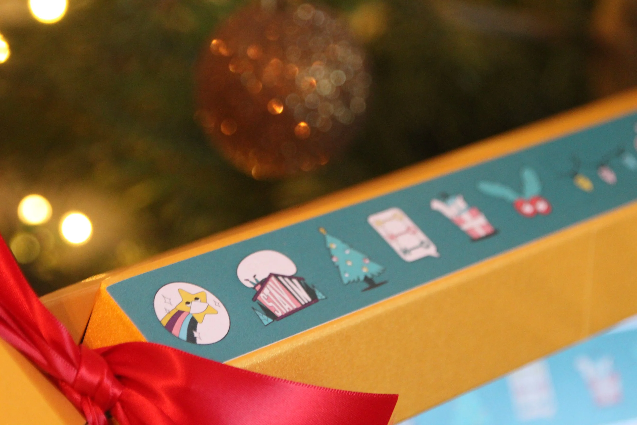 Close-up of a colorful holiday-themed game or toy box with a blue surface decorated with cartoon holiday icons and a red ribbon.