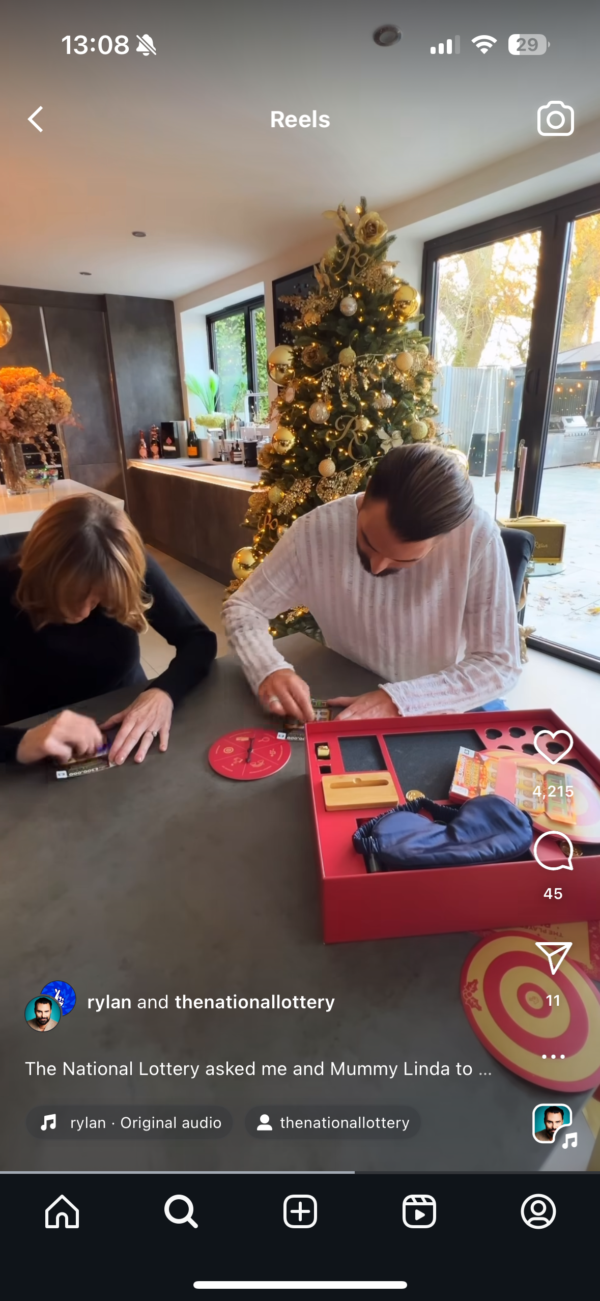 Two people playing a game at a table during Christmas time, with a decorated Christmas tree in the background near a large window.