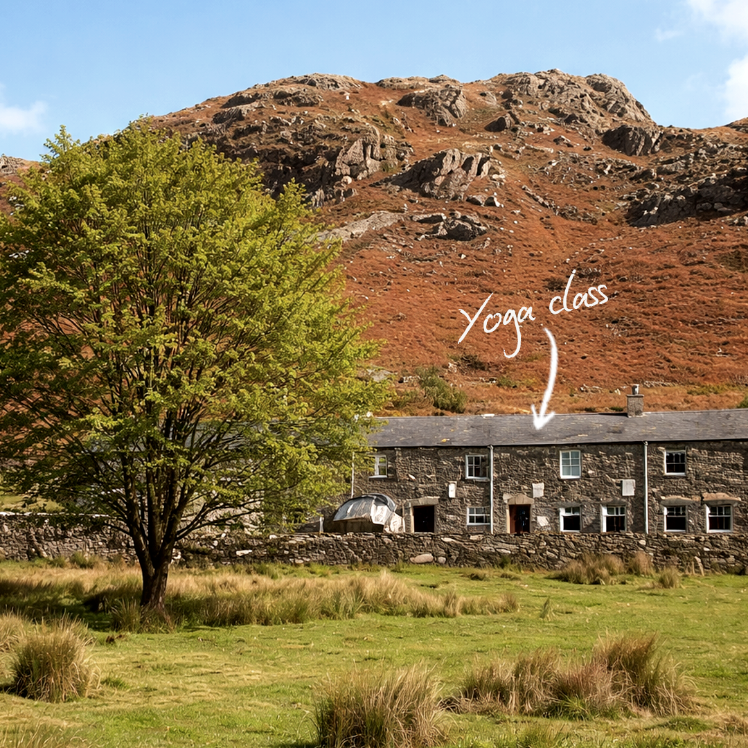 A grassy field with a large green tree in the foreground, a stone building with a slate roof labeled 'Yoga class' in the middle ground, and a rocky hill with sparse vegetation behind the building.