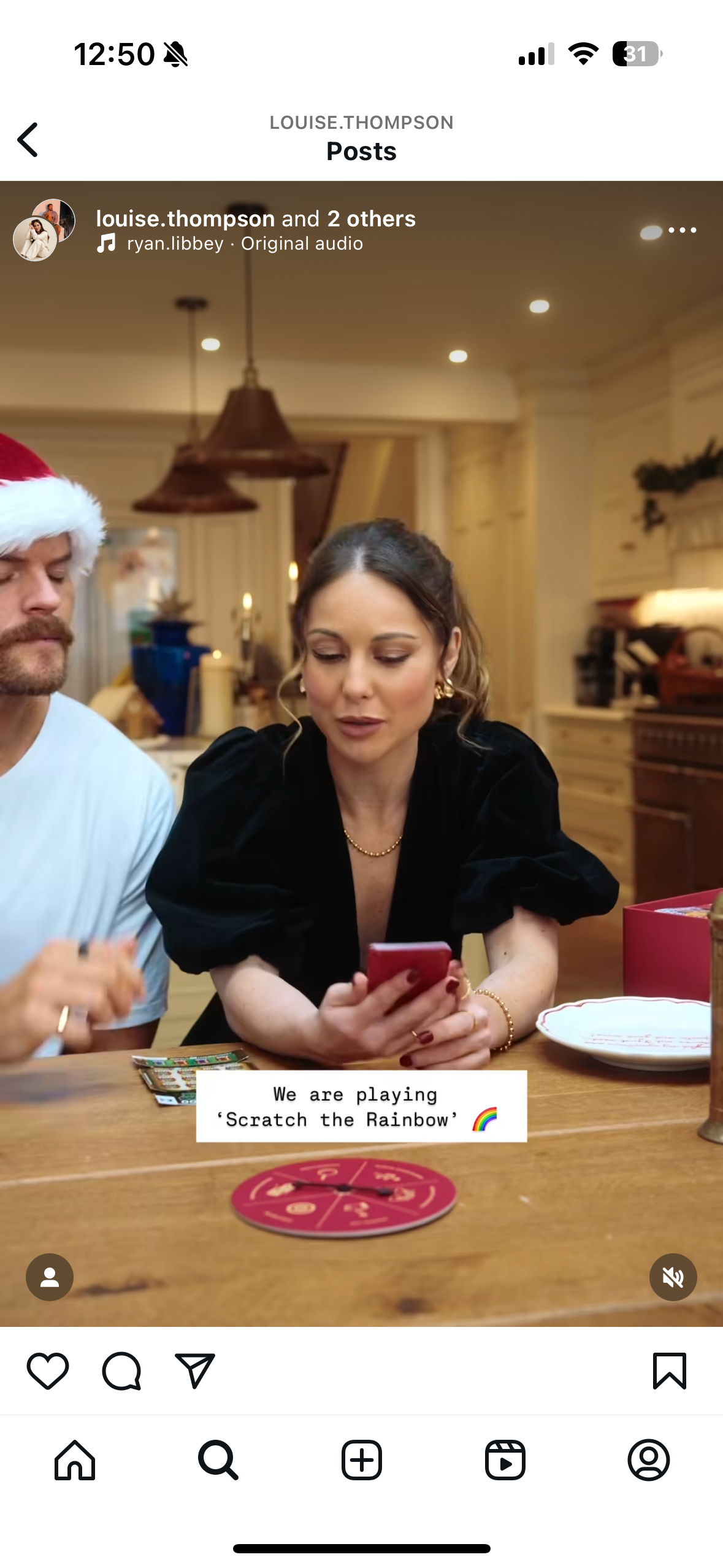 A woman and a man playing a game called 'Scratch the Rainbow' at a wooden table in a cozy, well-lit room decorated for the holidays, with candles and ornaments.