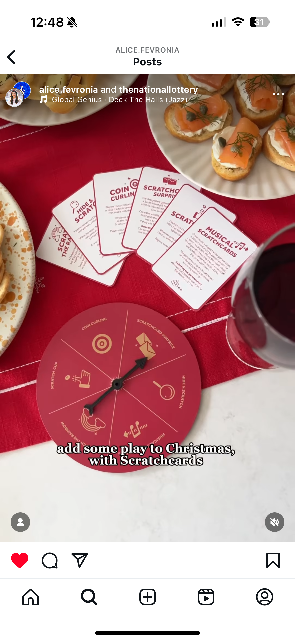 A red spinner wheel featuring game options such as "Coin Curling," "Scratchcard Surprise," "Hide & Scratch," "Musical Scratchcards," and "Scratch Cup." Surrounding the wheel are playing cards with instructions for a Christmas-themed game using scratch cards, placed on a red tablecloth with food and a glass of red wine nearby.
