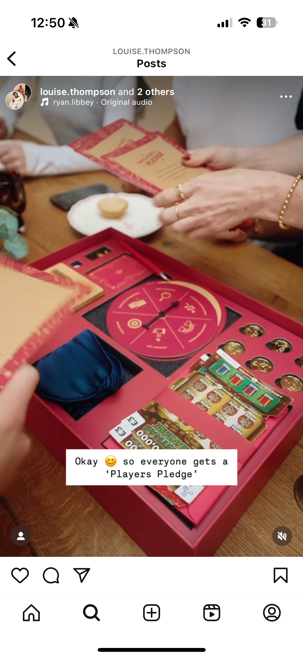 A group of people gathered around a table playing a board game called 'Players Pledge', which includes a spinning wheel and scratch-off cards. The board game box is open, displaying various game components, and a small plate with a snack is on the table.