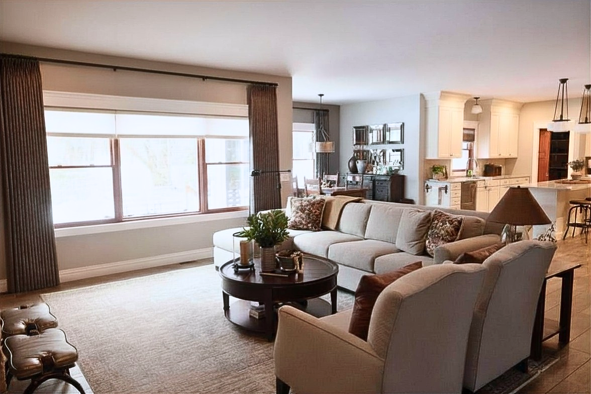 Transitional style open space with living room, dining room and kitchen.  Neutral sectional with chaise. Accent chairs in performance fabric. Craftsman style lighting in ivory kitchen. Darkwood furniture and medium stain floors. Featherstone.