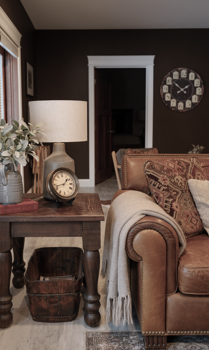 Chocolate brown basement media room with leather sofa and rustic style side table.