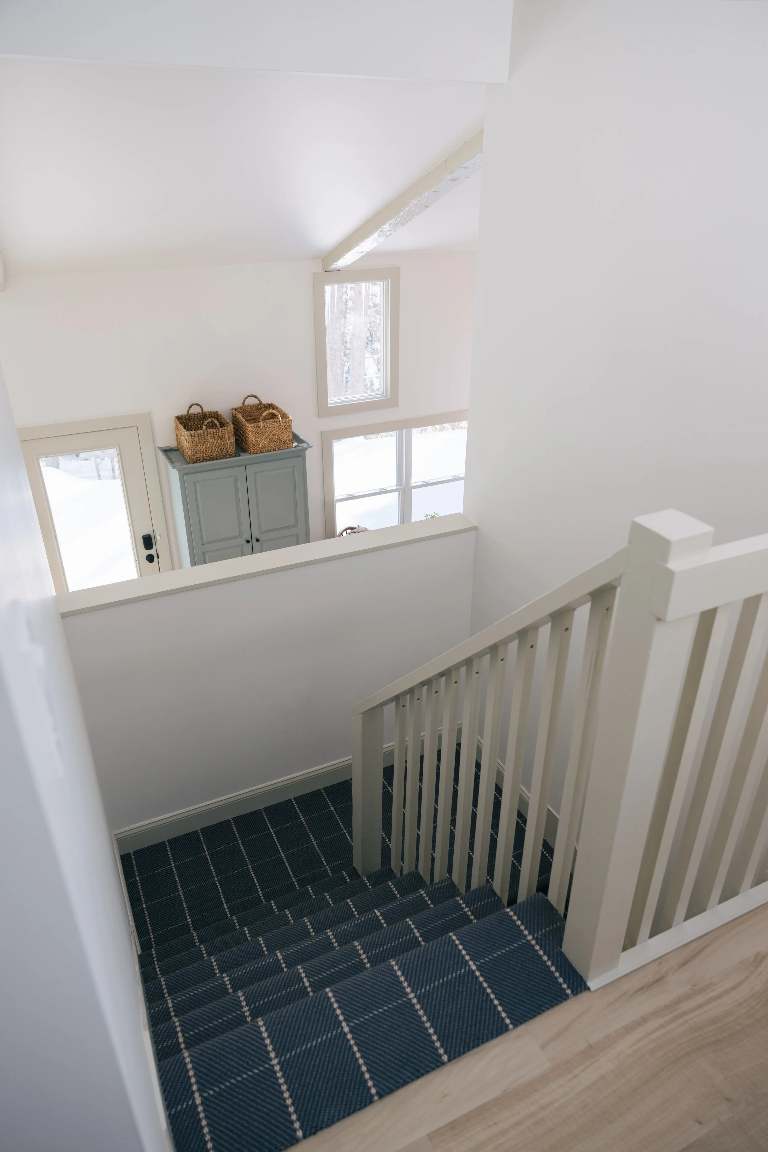 Bright stairwell at Pine & Plaid cabin in Quechee, Vermont viewed from the staircase, featuring large windows, modern finishes, and welcoming storage for family stays.