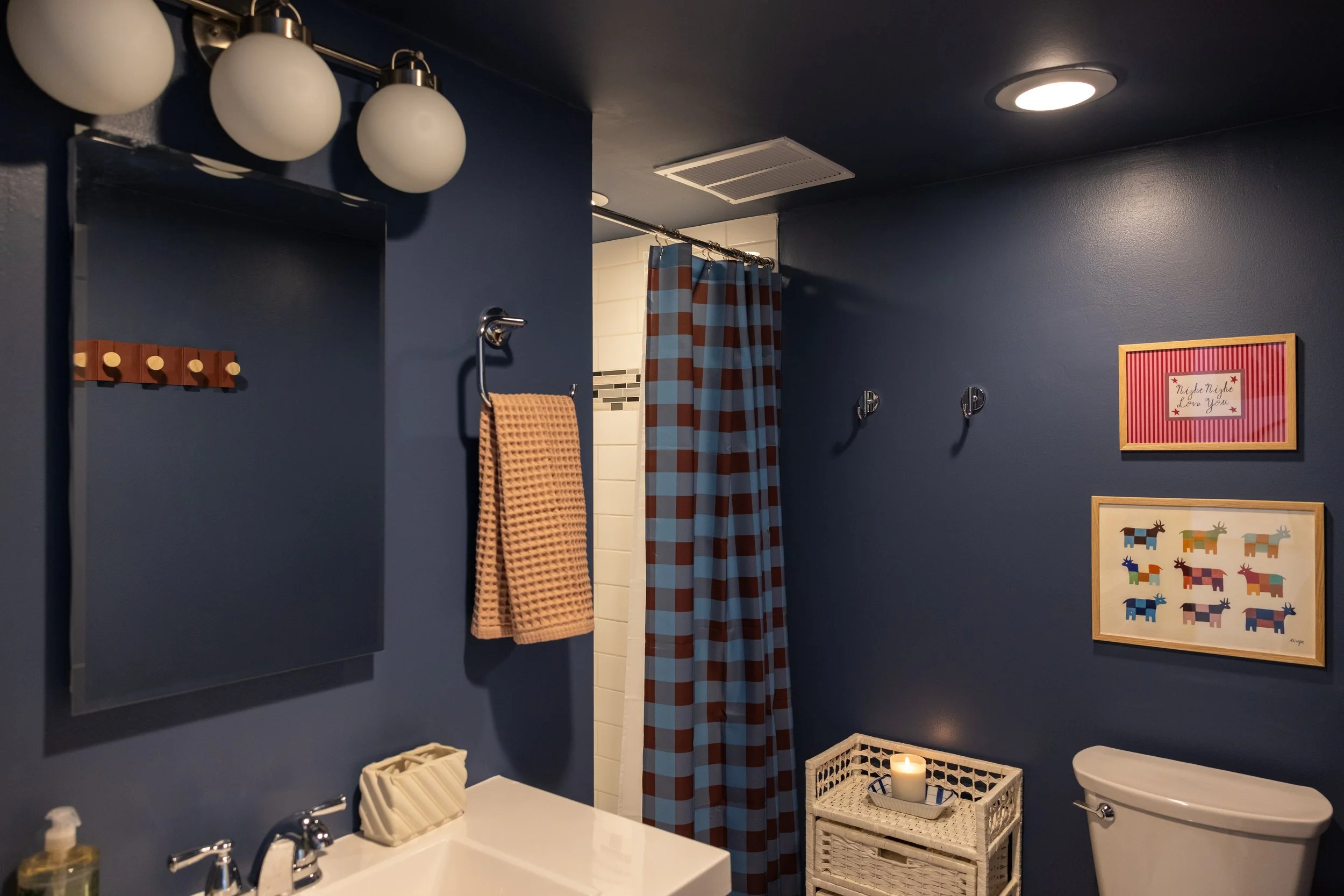 Navy blue bathroom at Pine & Plaid Vermont cabin rental with white sink, colorful artwork, and full shower — ideal for comfortable multi-generational family getaways.