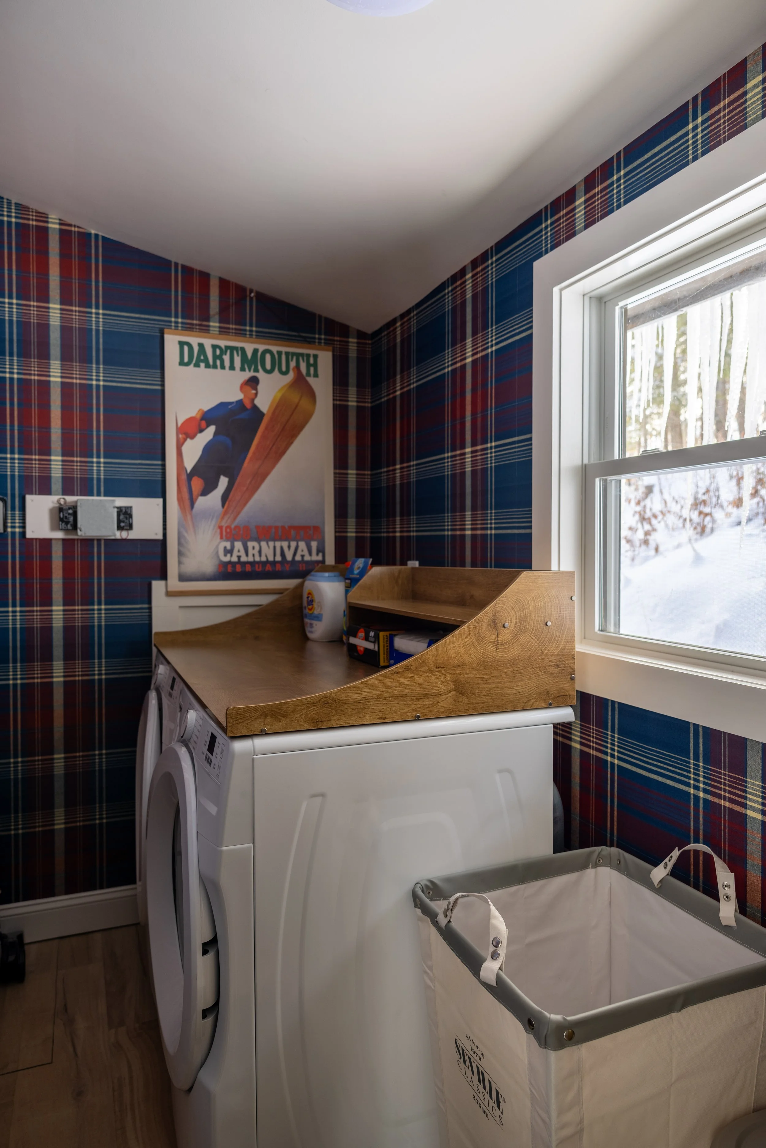 Laundry room at Pine & Plaid vacation cabin in Quechee, Vermont with washer and vintage Dartmouth poster.
