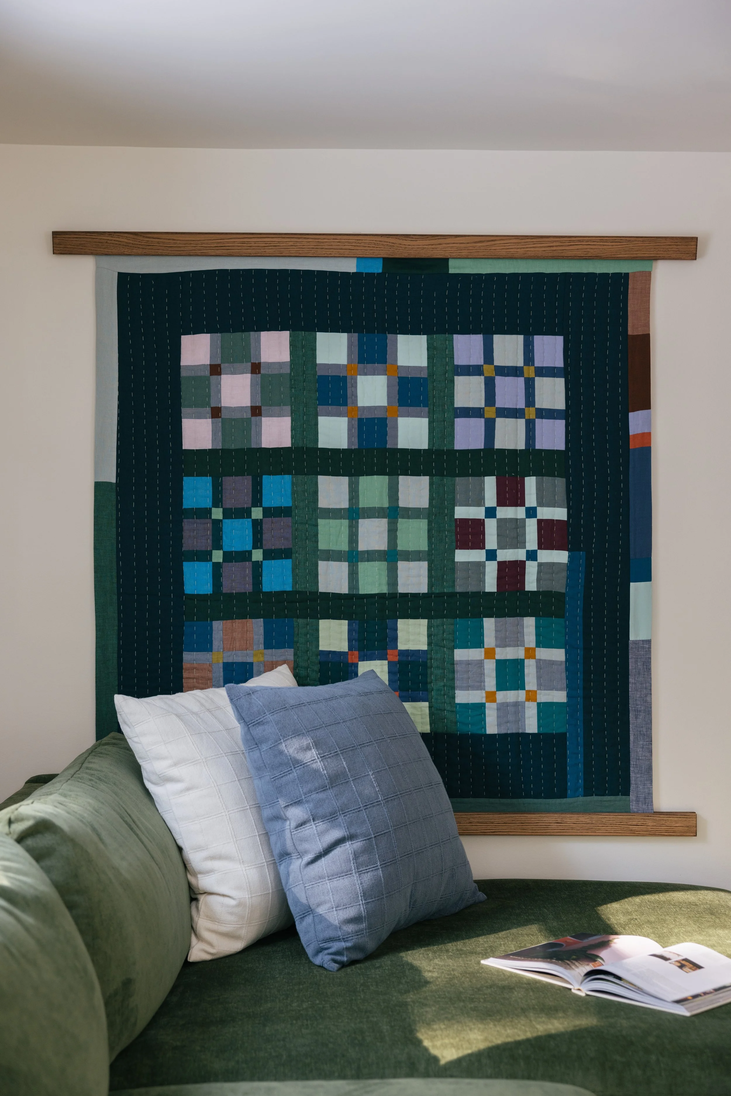 Cozy living room at Pine & Plaid cabin in Quechee, Vermont featuring a green sofa, colorful quilt wall art, and inviting seating for a relaxing family getaway.