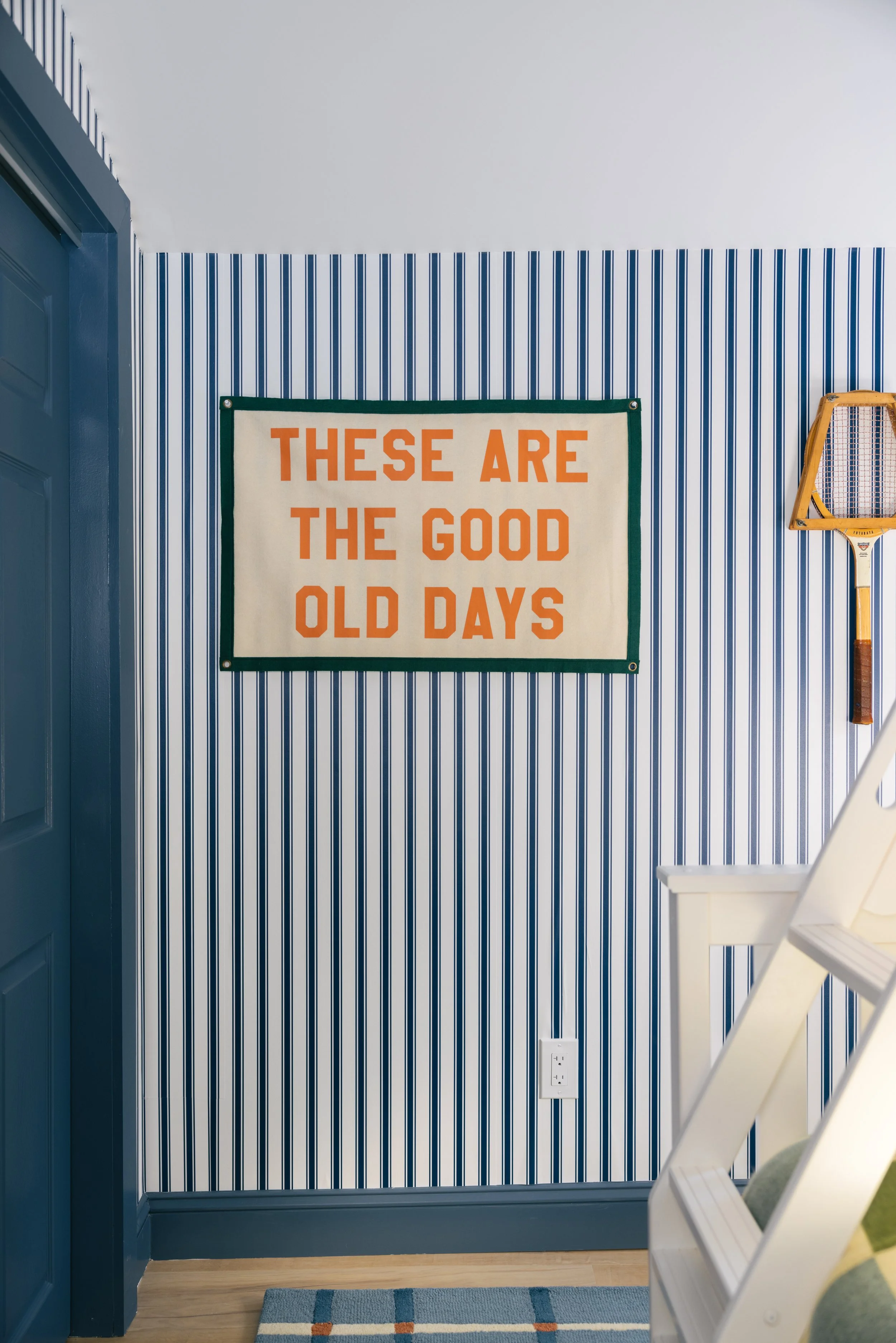 Blue and white striped accent wall at Pine & Plaid cabin in Quechee featuring vintage tennis decor and “These Are the Good Old Days” artwork.