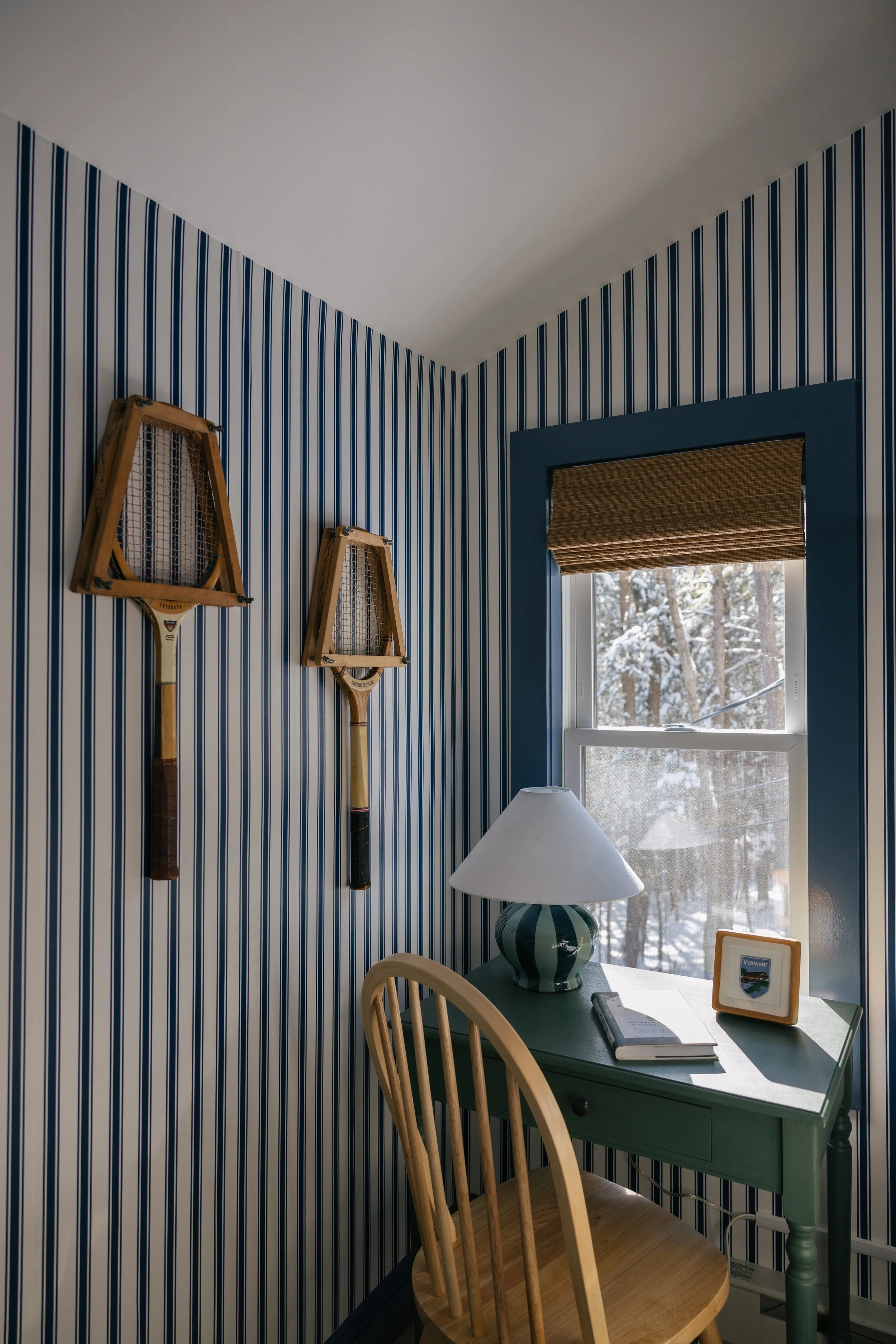 Cozy reading nook at Pine & Plaid cabin in Quechee, Vermont with blue and white striped walls, vintage tennis decor, green writing desk, and snowy winter views.