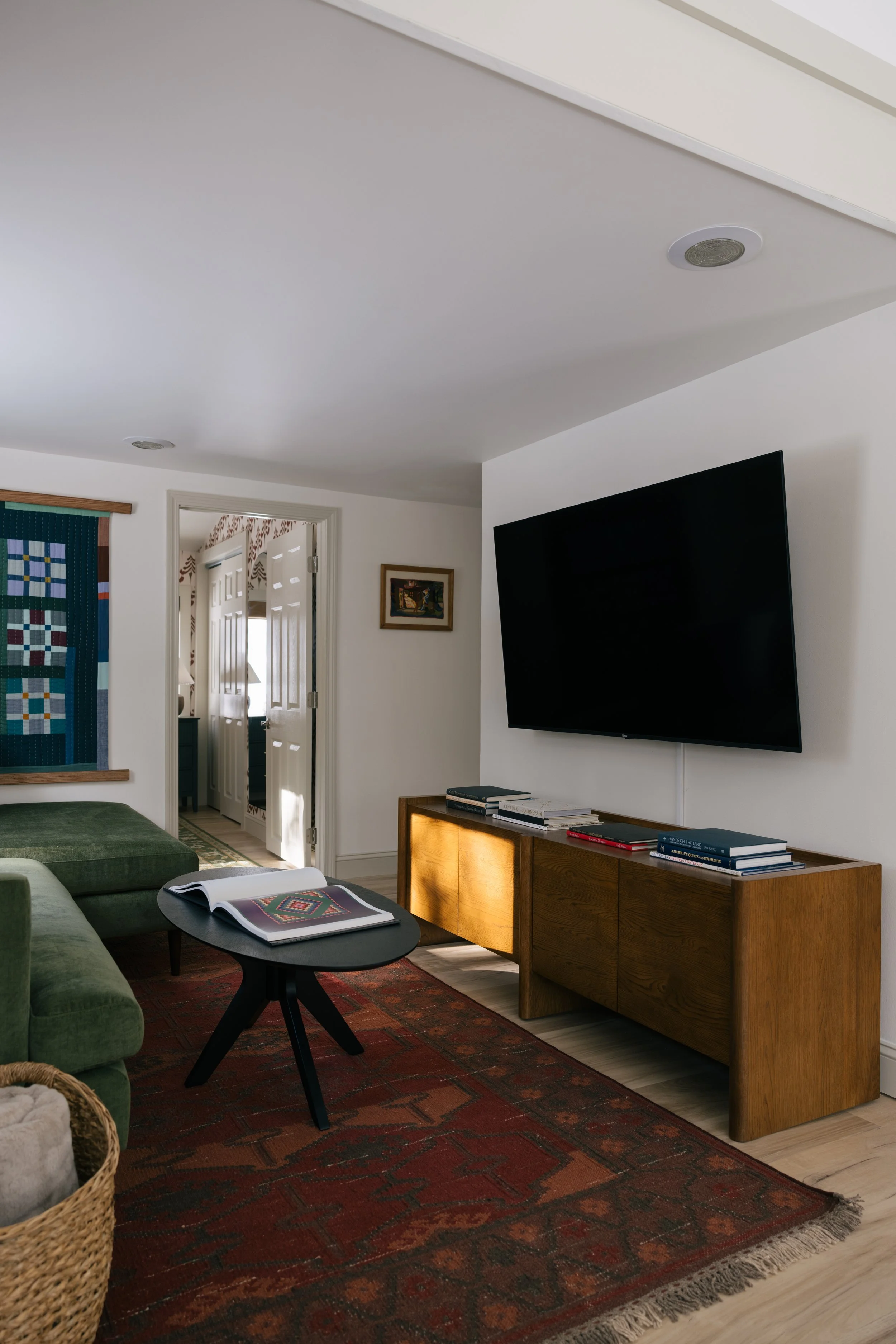 Inviting living room at Pine & Plaid Vermont cabin rental featuring green velvet sofa, wall-mounted TV, warm wood accents, and comfortable seating for family movie nights.