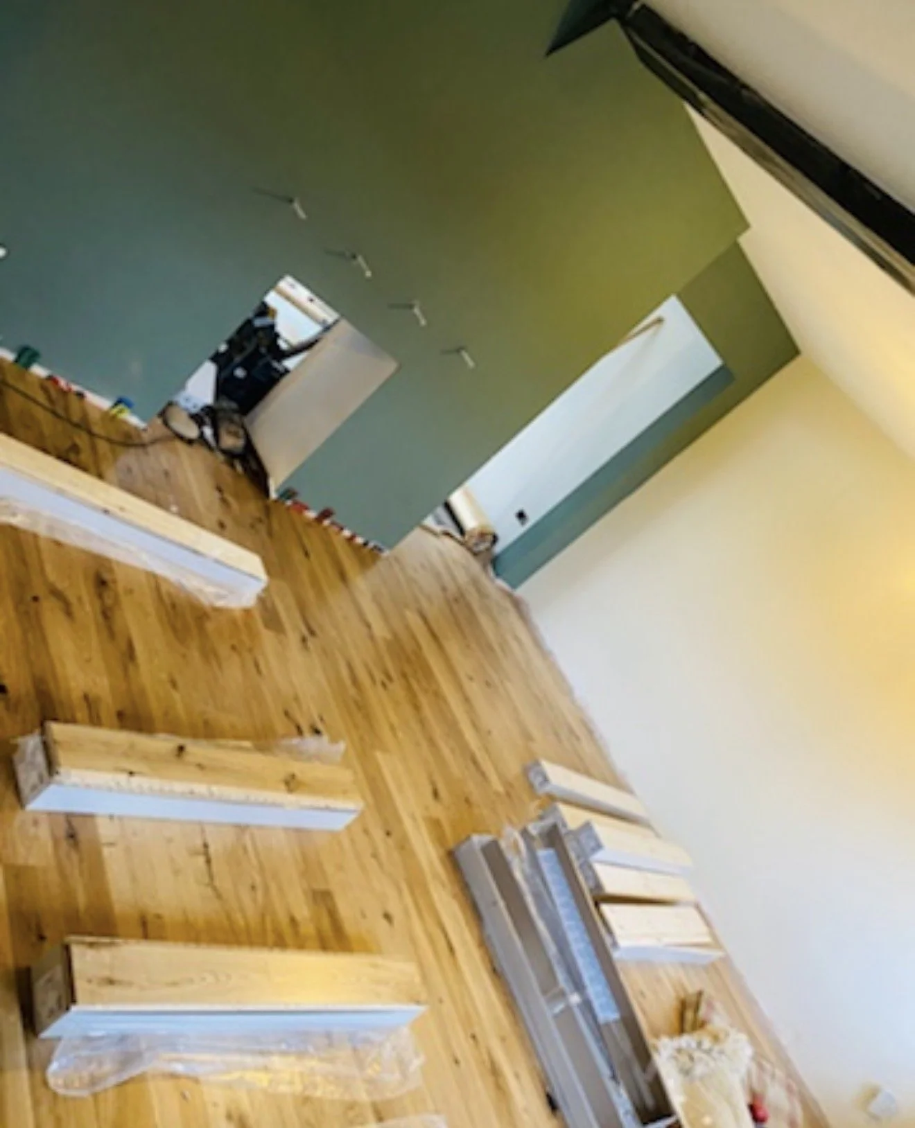 Interior of a room under renovation with wooden floor, scattered wood pieces, and green and beige painted walls.
