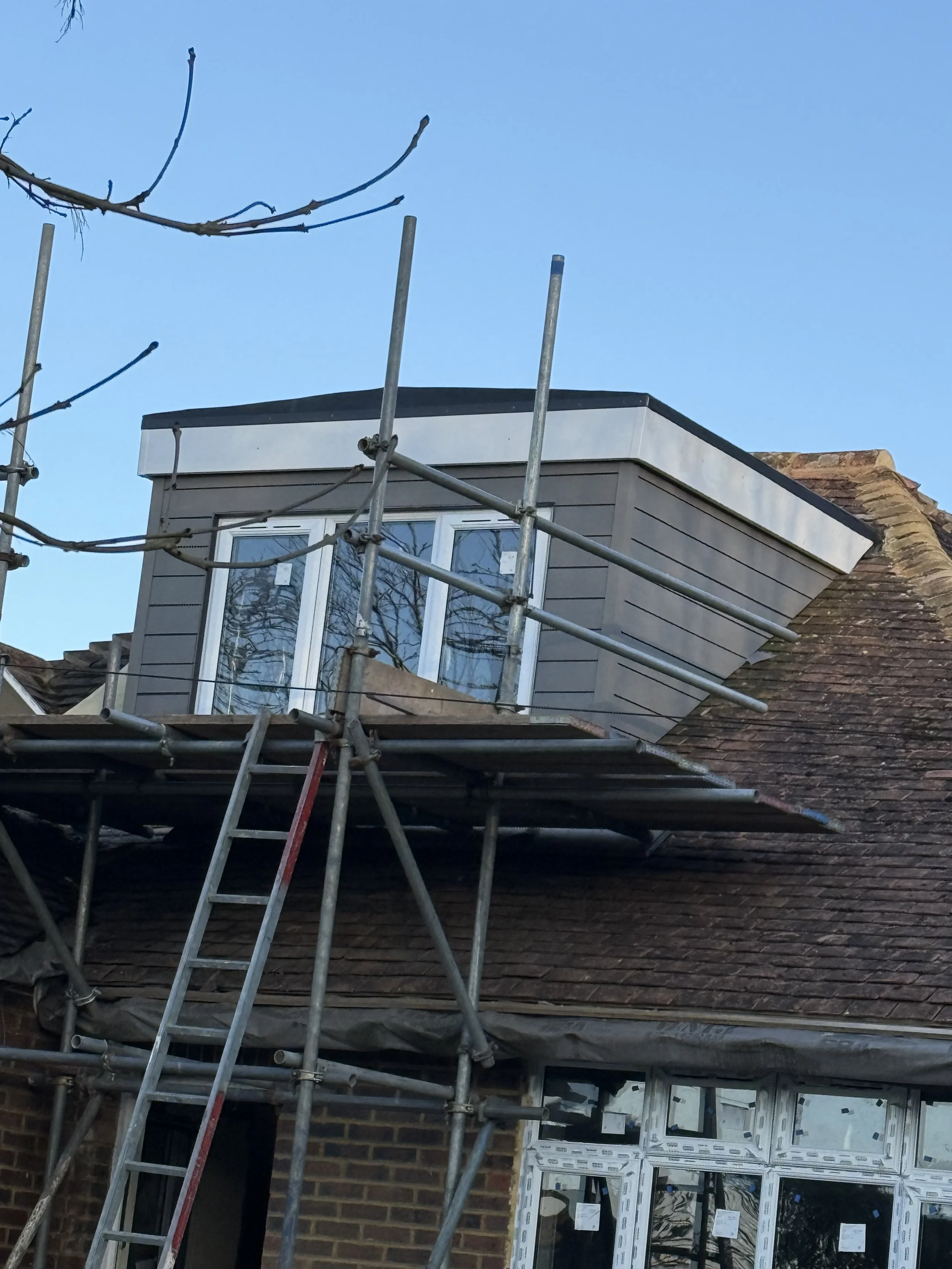 House under renovation with scaffolding, new window installed in the upper floor, and a clear blue sky in the background.