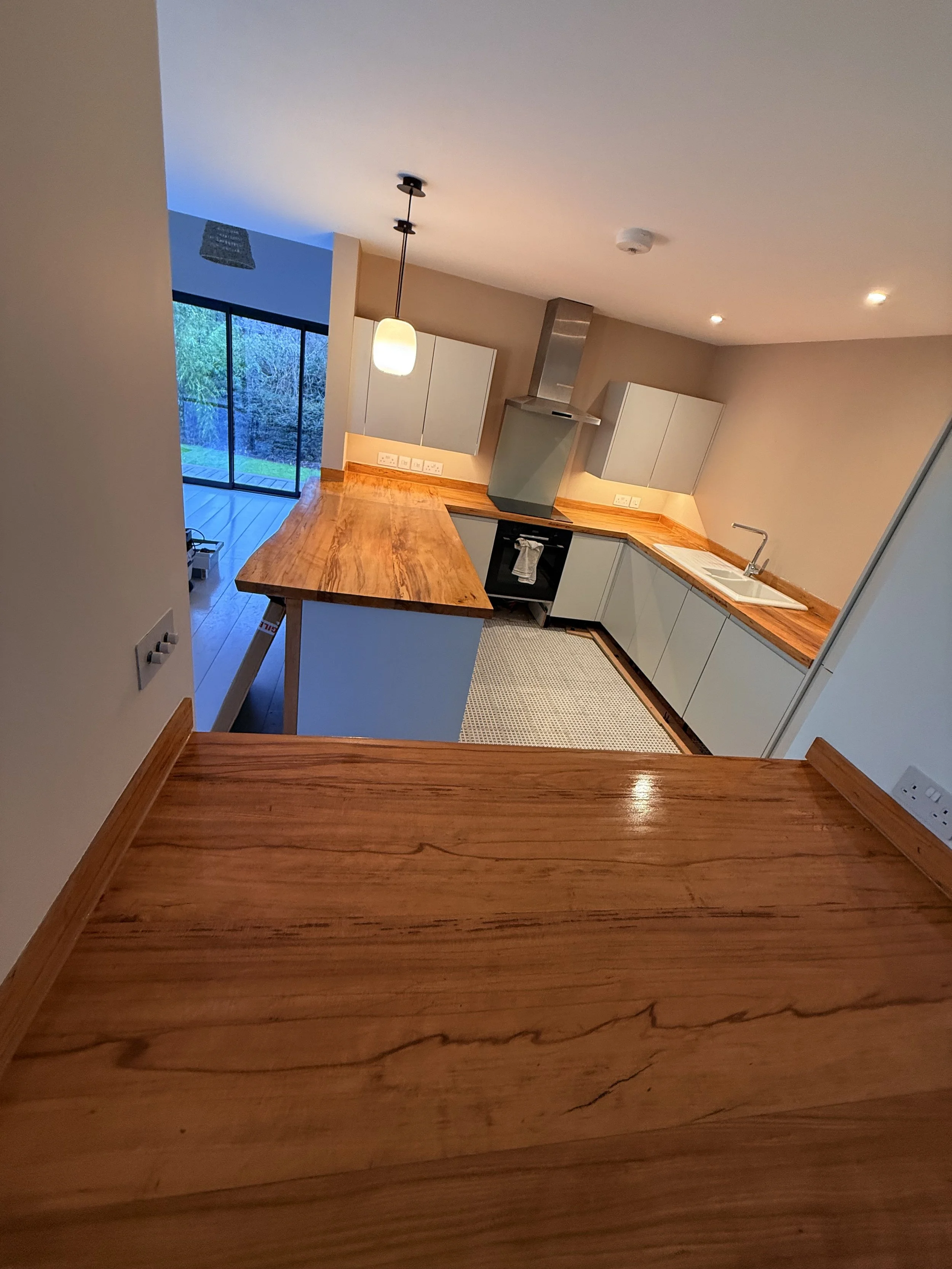 View of a modern kitchen with wood countertops, white cabinetry, stainless steel oven and range hood, and a sliding glass door leading to an outdoor area.