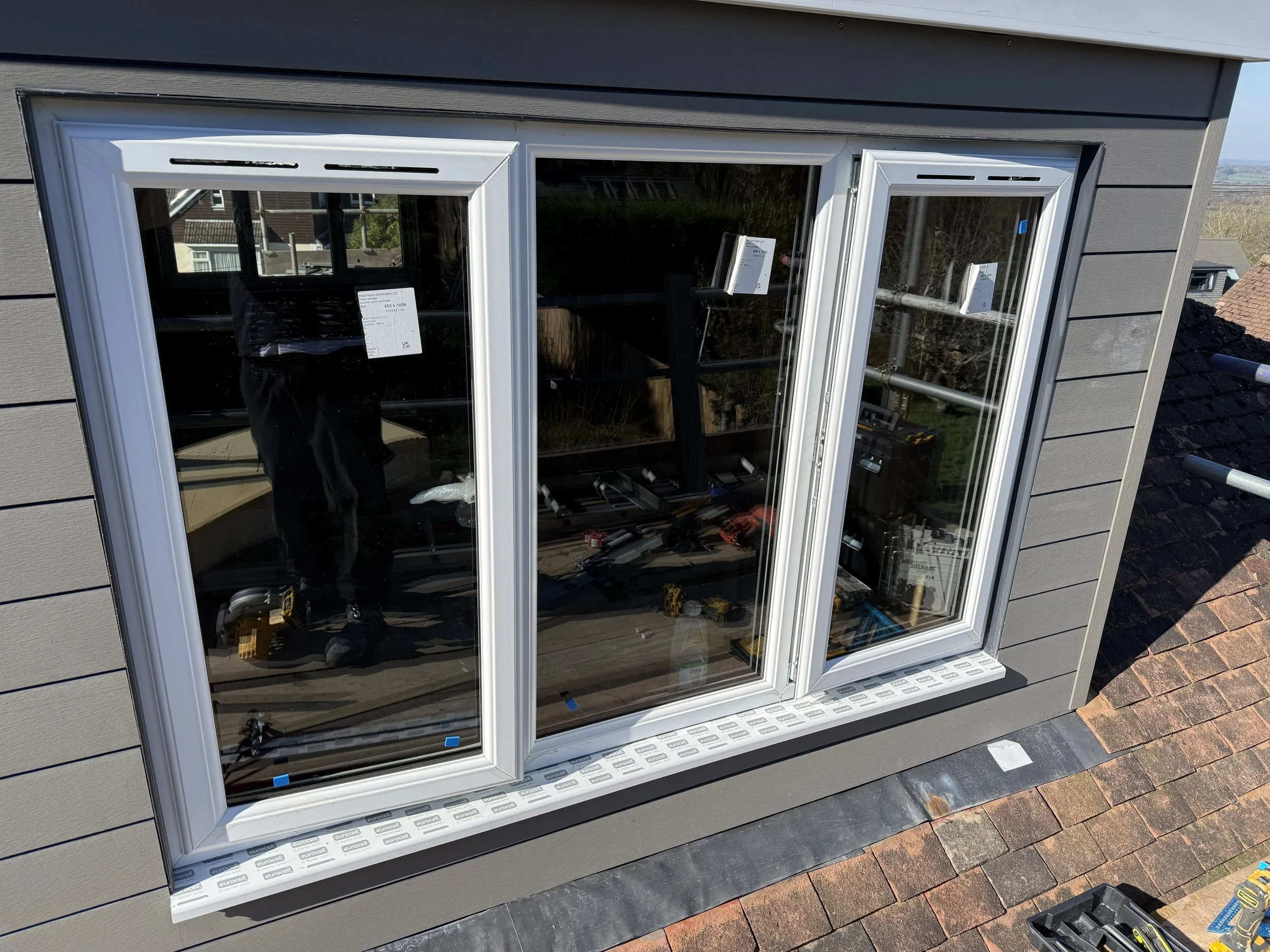 Newly installed double-pane window on second floor of house, with tools and construction materials nearby.