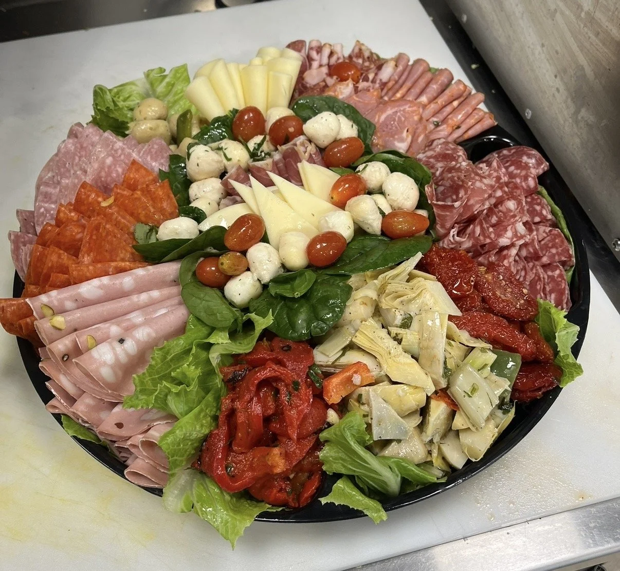 Assorted cold cut meats, cheese, fresh mozzarella, grape tomatoes, basil, arugula, and marinated vegetables on a large platter.